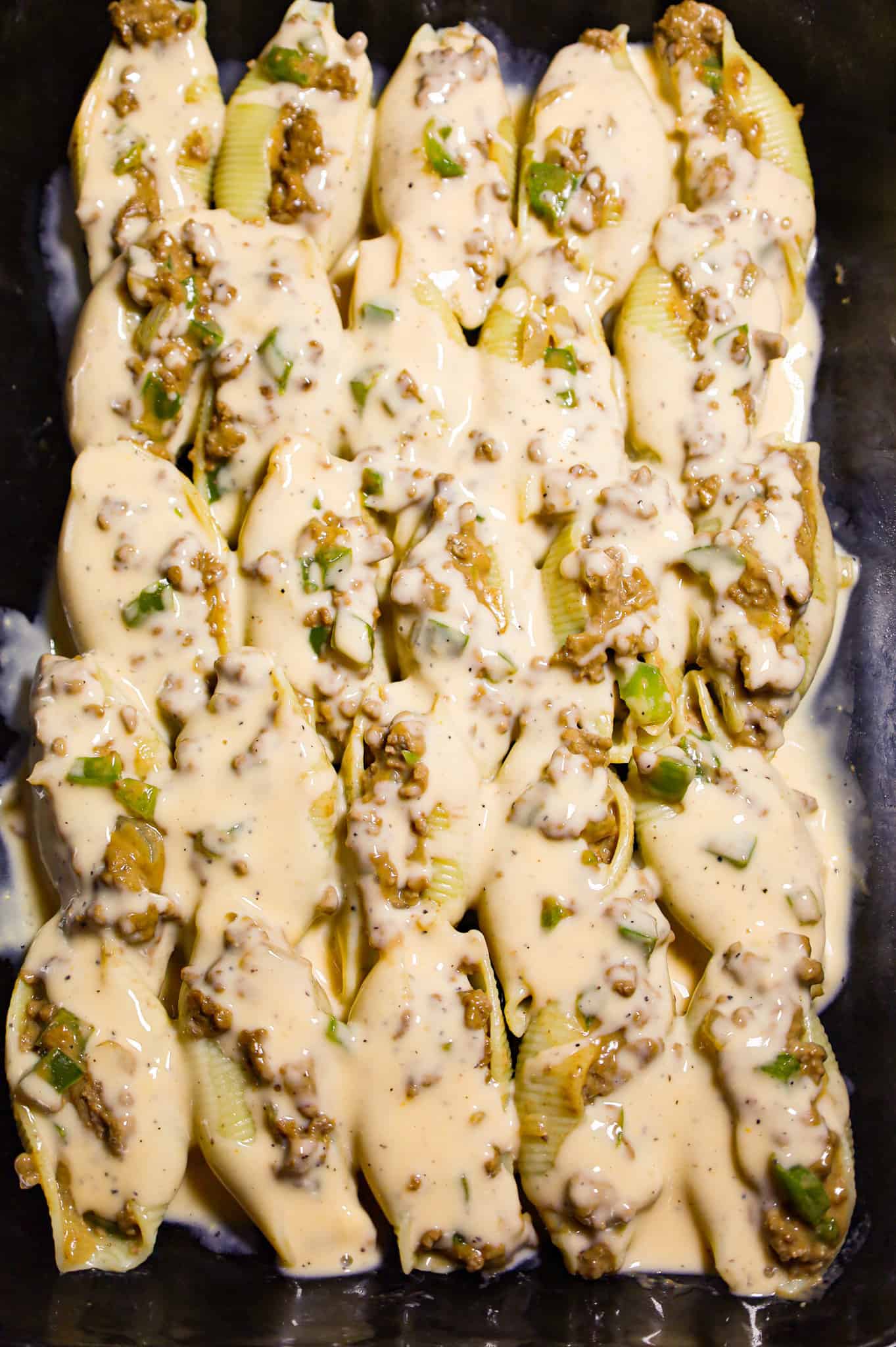 cheddar sauce poured over stuffed shells in a baking dish