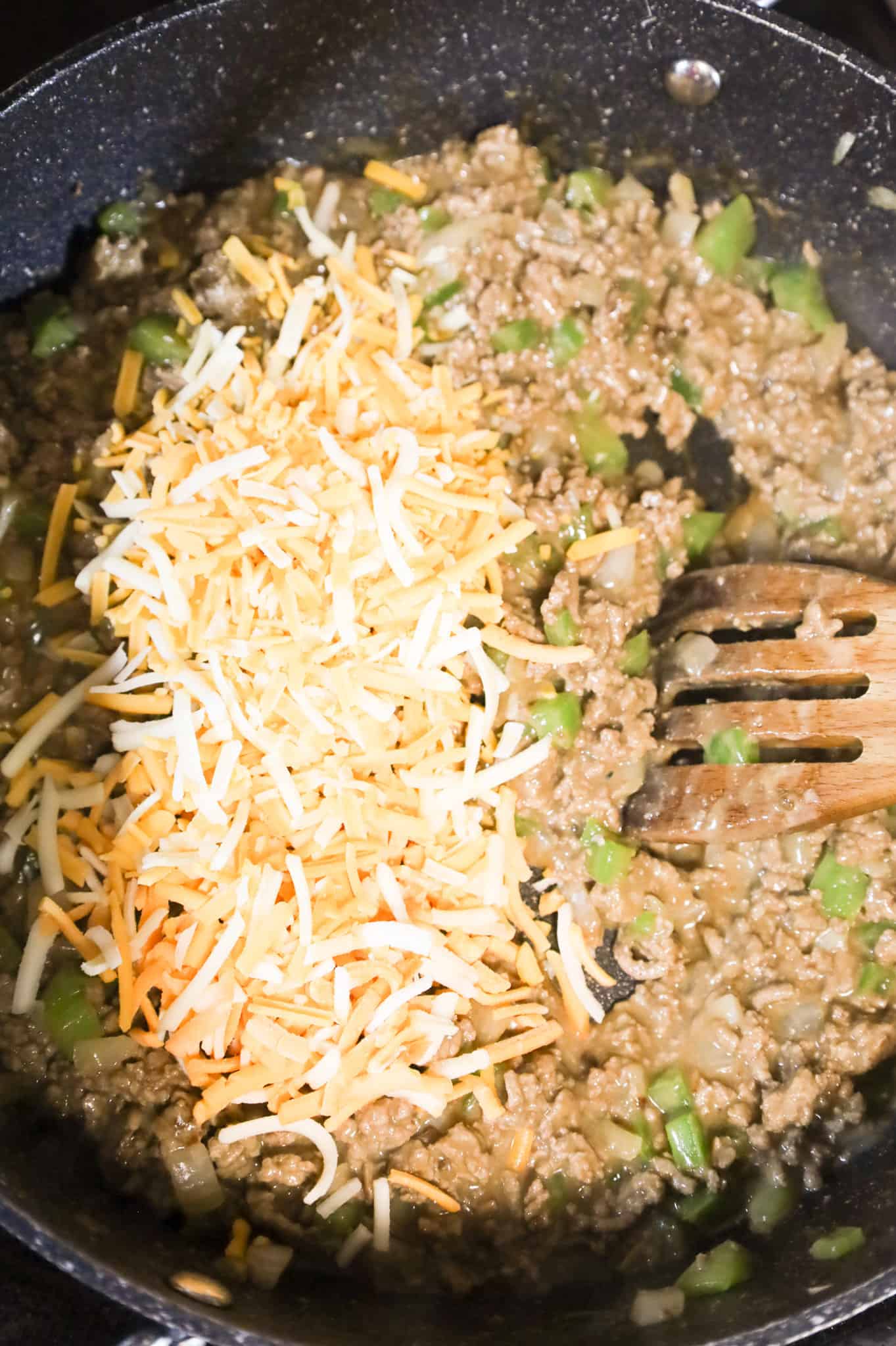 shredded cheese added to ground beef and cheddar soup mixture in a skillet