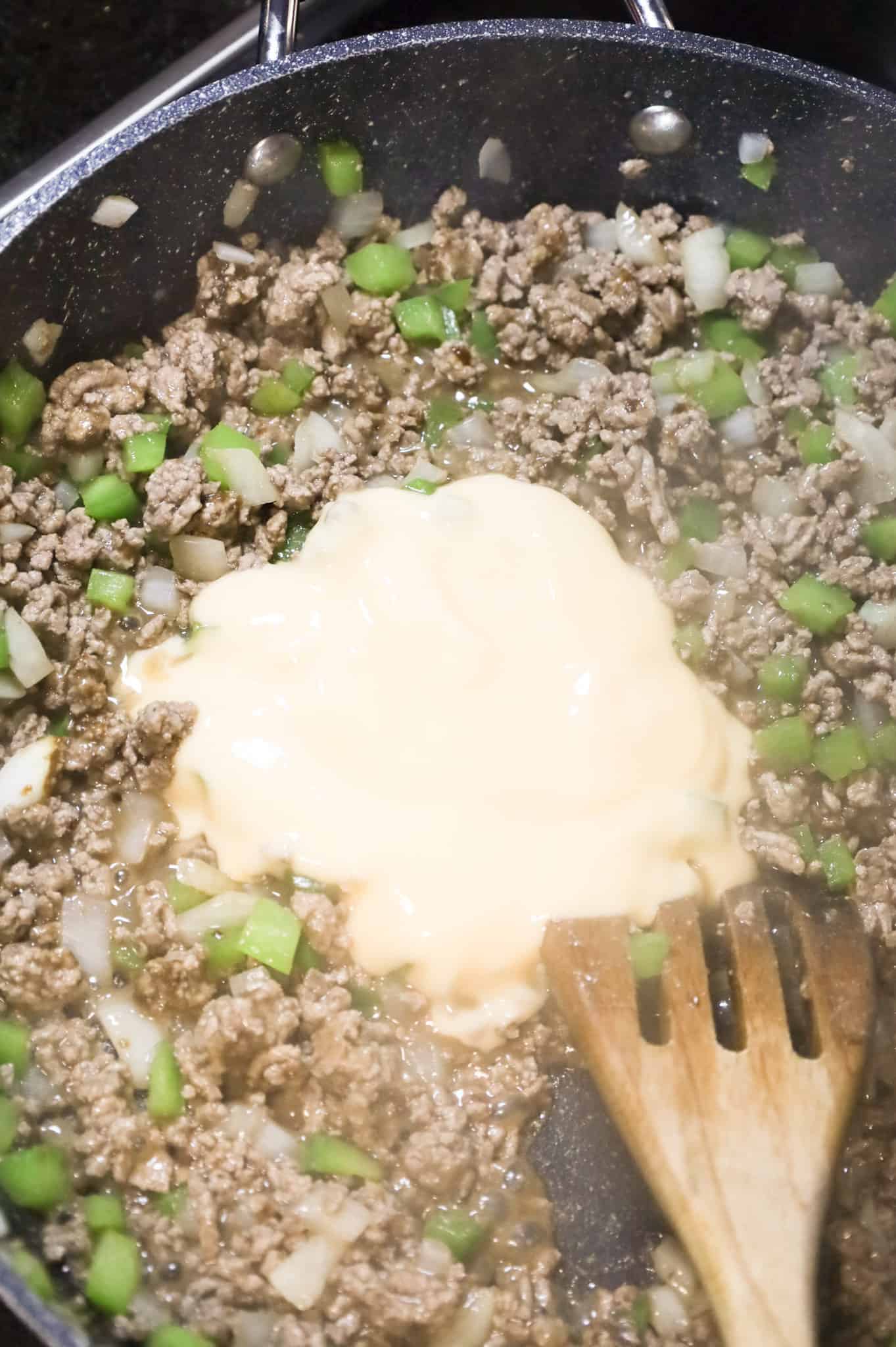 condensed cheddar cheese soup on top of ground beef, diced onions and green peppers in a skillet