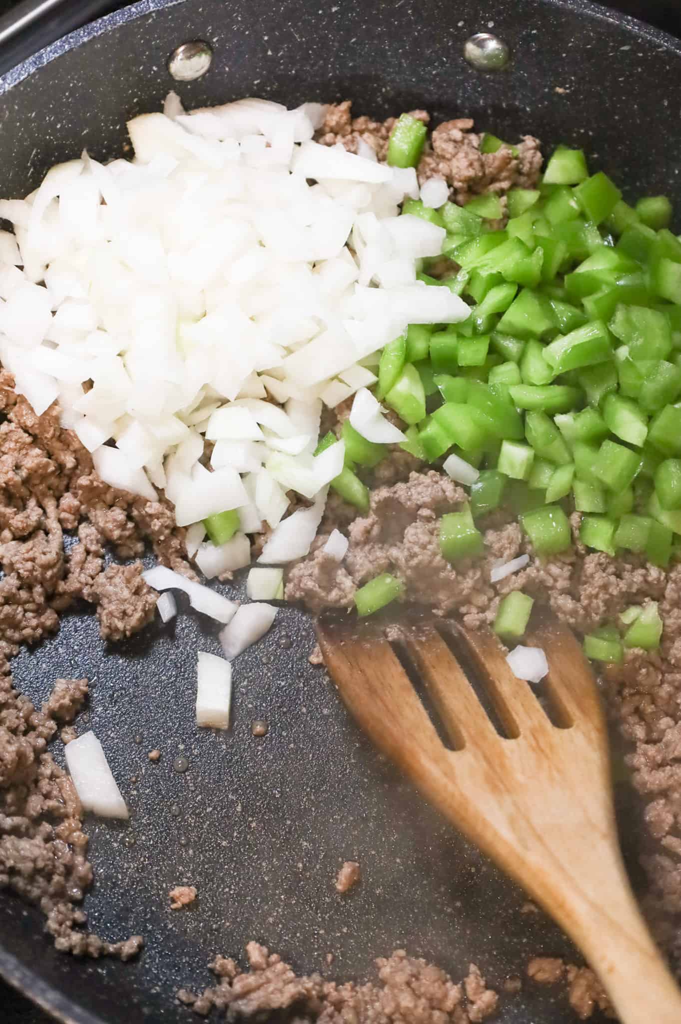 diced onions and diced green peppers on top of cooked ground beef in a skillet
