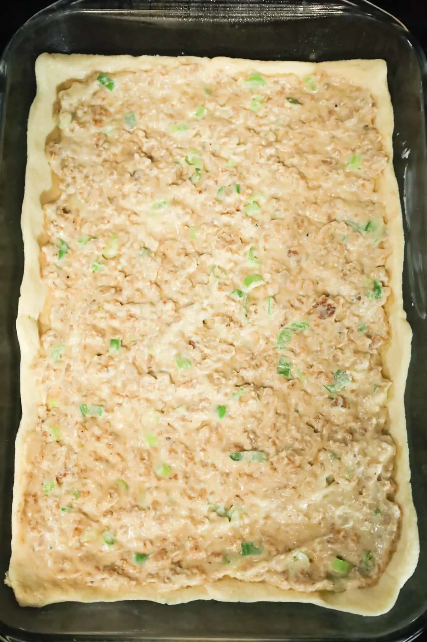 cream cheese and sausage mixture on top of crescent dough in a baking dish
