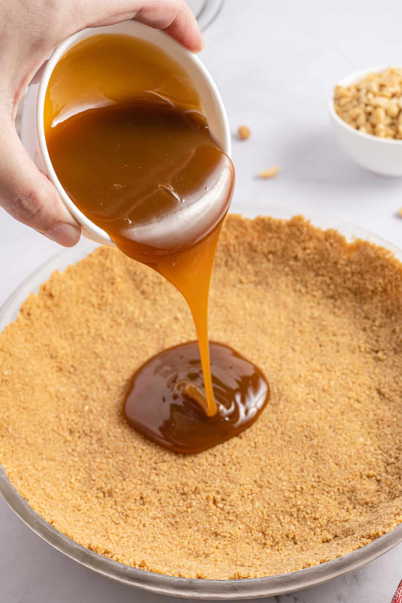 caramel sauce being poured into a graham pie crust