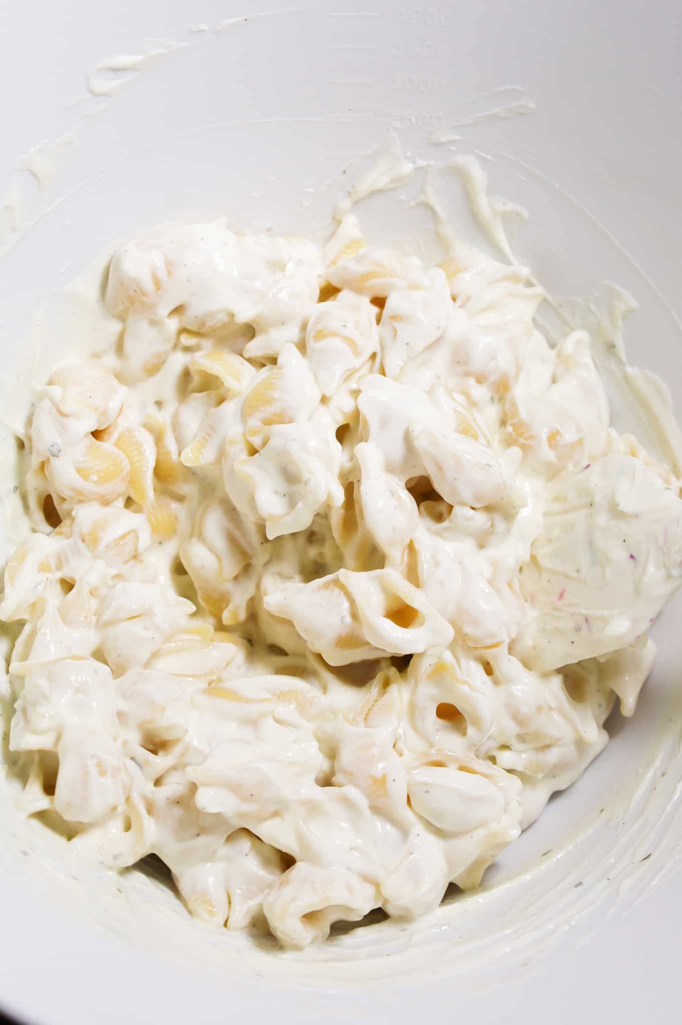 shell pasta tossed in sour cream and cream cheese mixture in a mixing bowl
