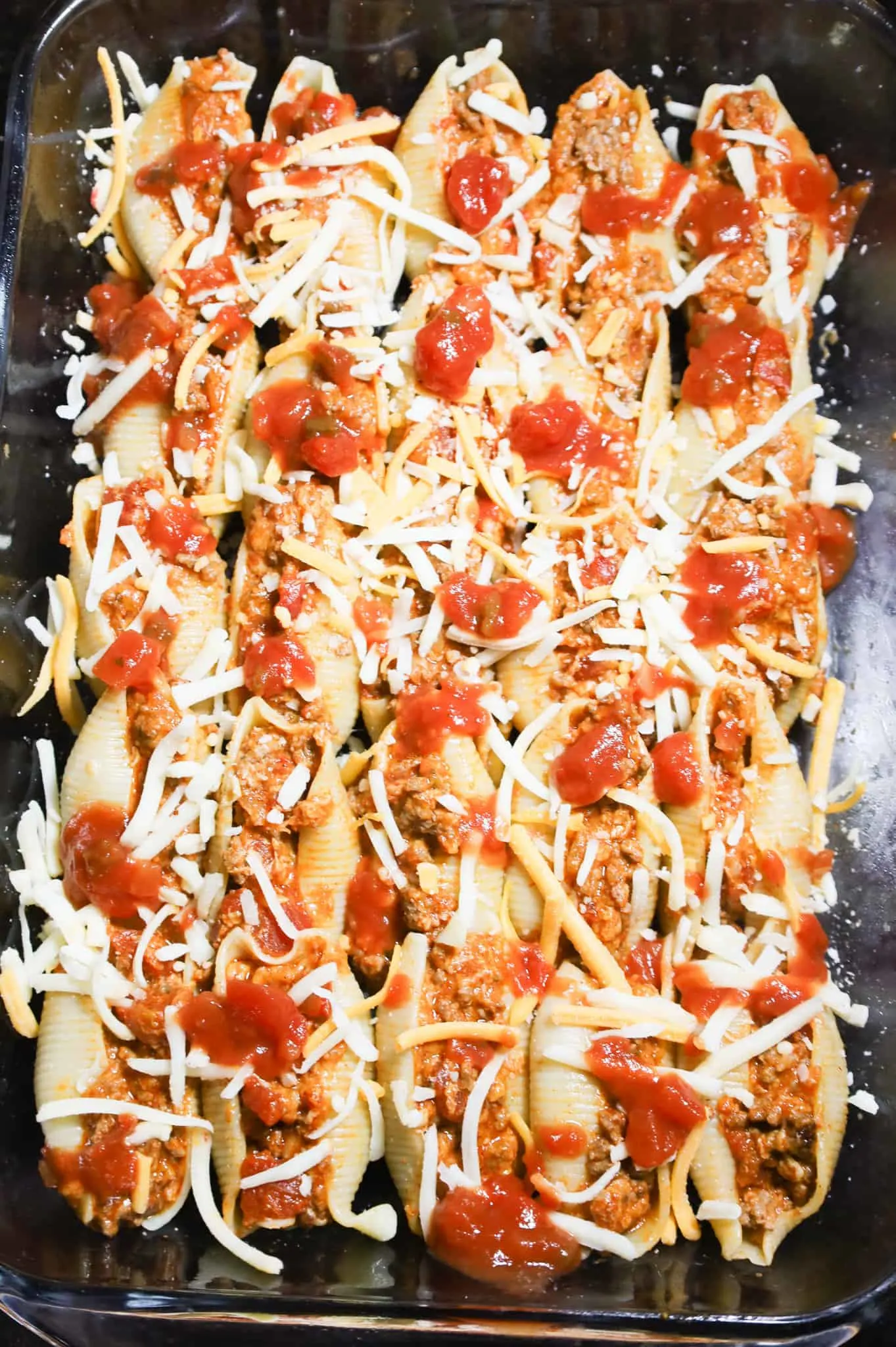 salsa and shredded cheese on top of taco stuffed shells on top of a baking dish