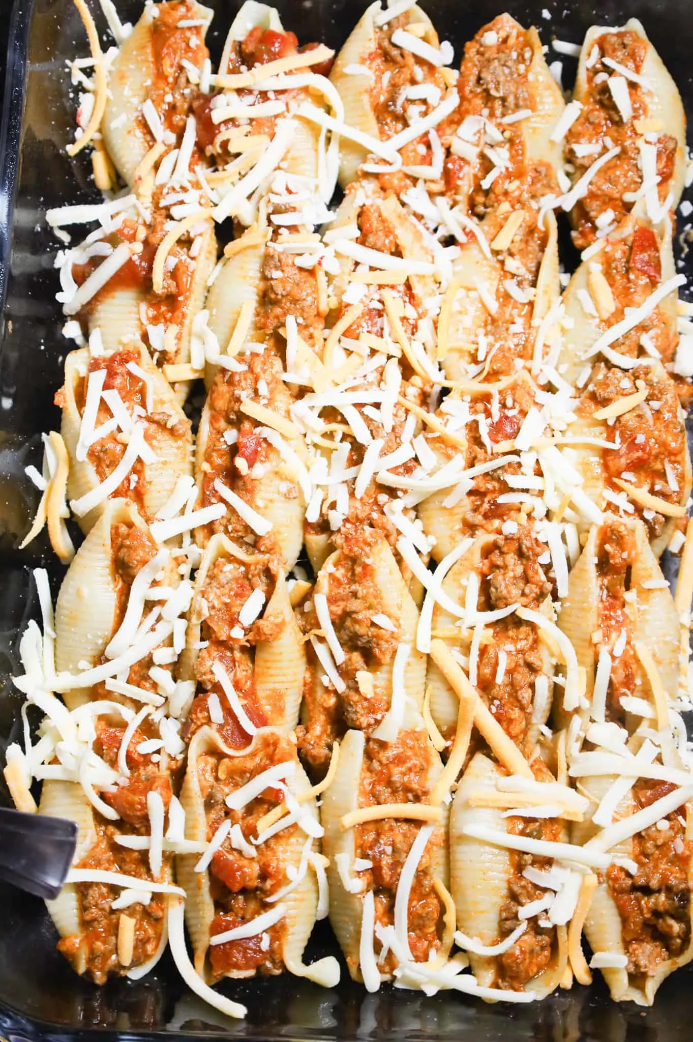 shredded cheese on top of stuffed pasta shells in a baking dish