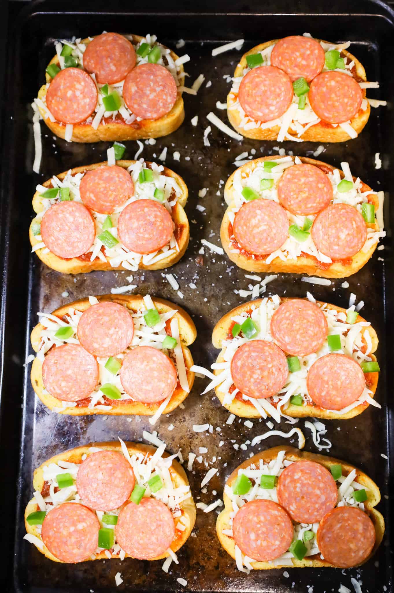 diced green peppers and pepperoni slices on top of shredded cheese on texas toast slices on a baking sheet