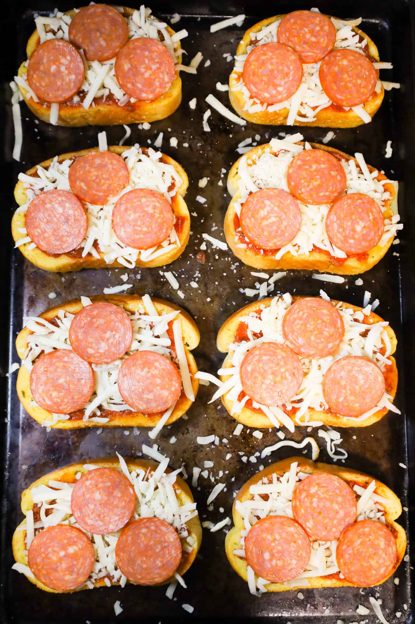 pepperoni slices, mozzarella cheese and pizza sauce on top of garlic texas toast slices on a baking sheet