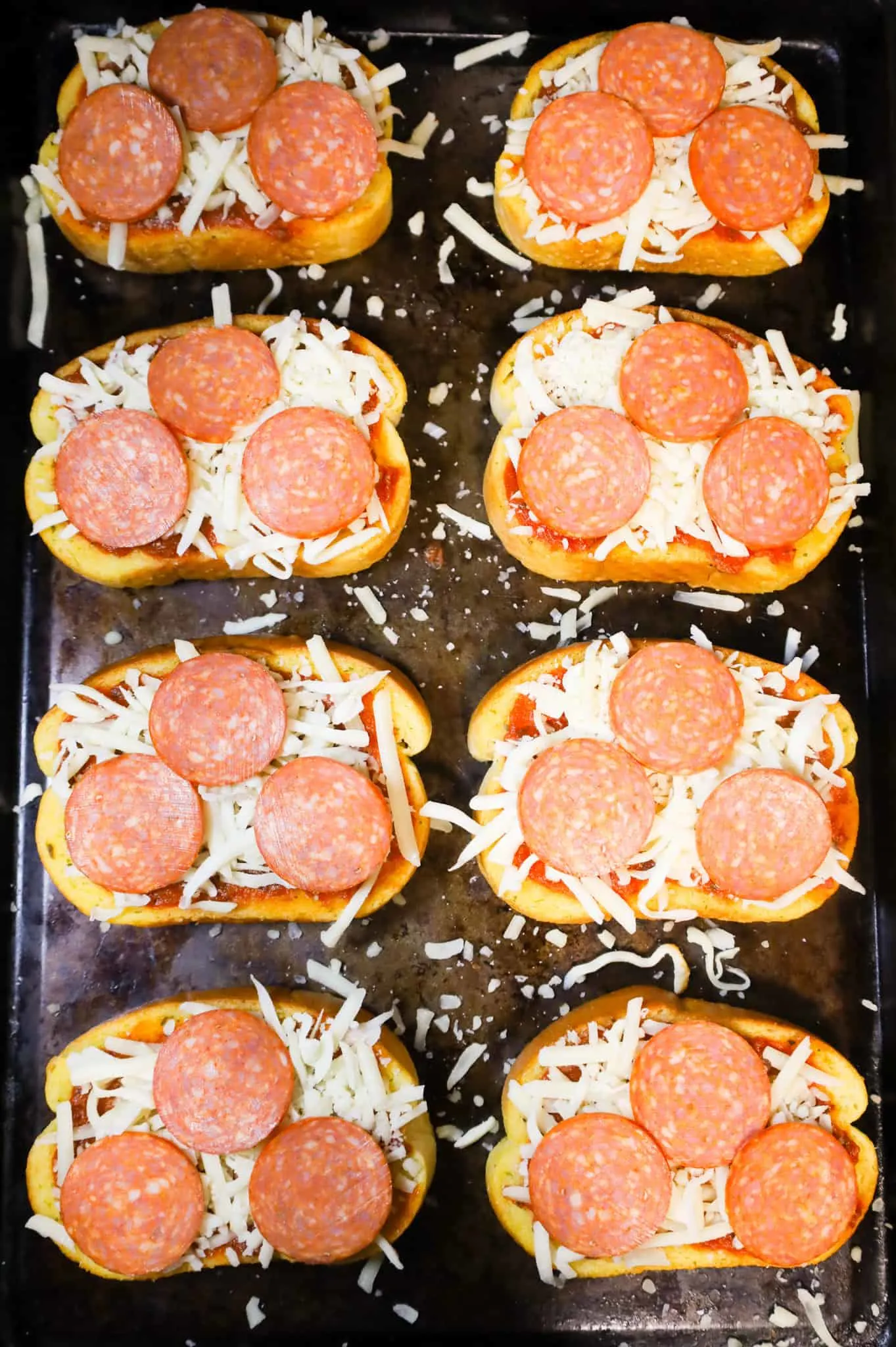 pepperoni slices, mozzarella cheese and pizza sauce on top of garlic texas toast slices on a baking sheet
