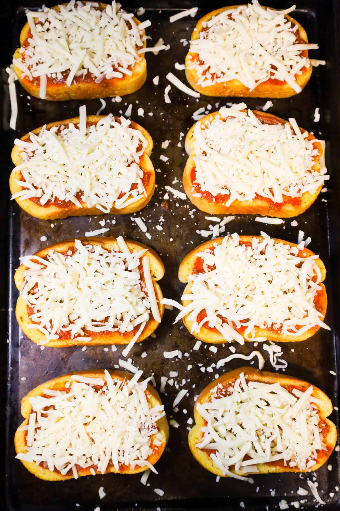 shredded mozzarella cheese and pizza sauce on top of slices of garlic texas toast on a baking sheet