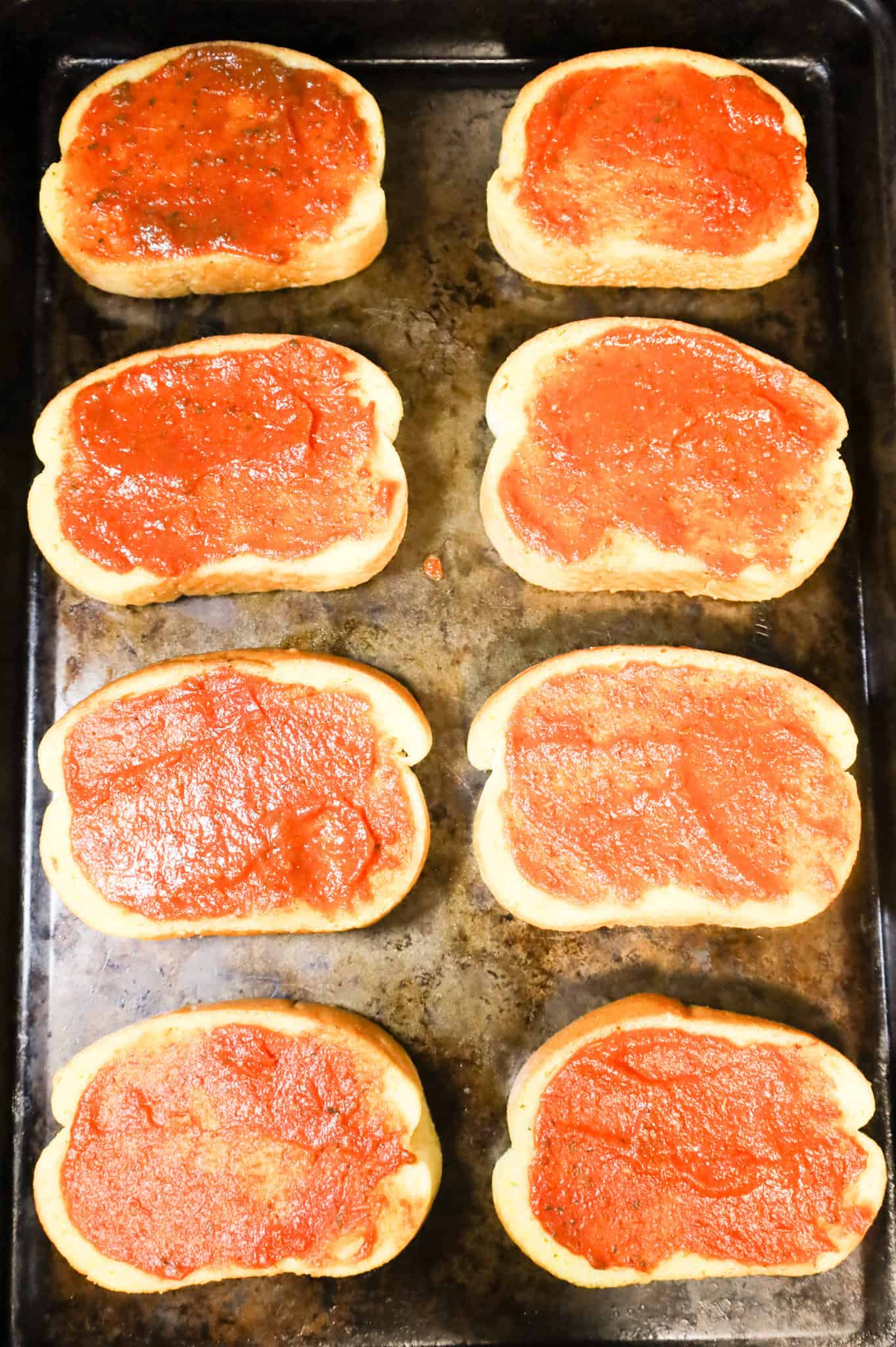 pizza sauce spread on garlic Texas toast slices on a baking sheet