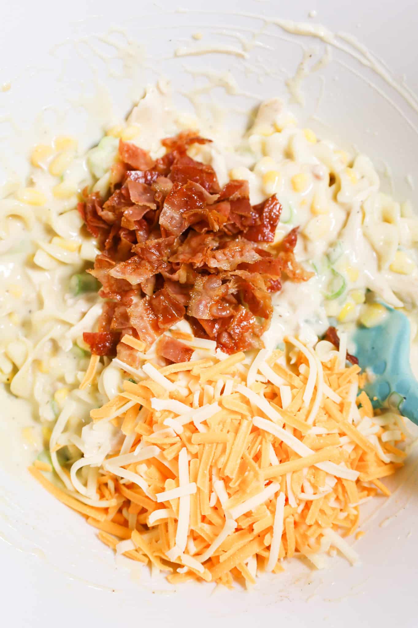 chopped bacon and shredded cheese on top of creamy chicken noodle mixture in a mixing bowl