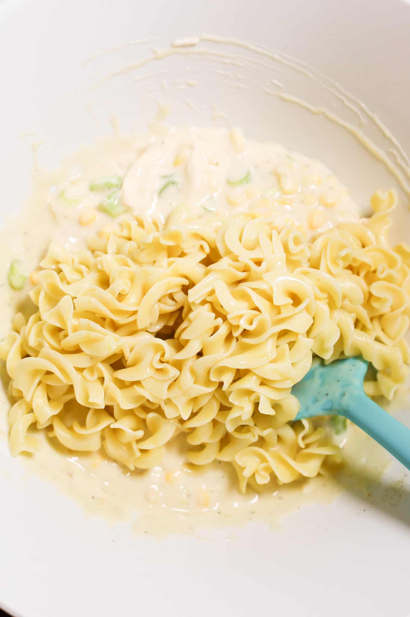 cooked egg noodles on top of creamy soup mixture in a mixing bowl