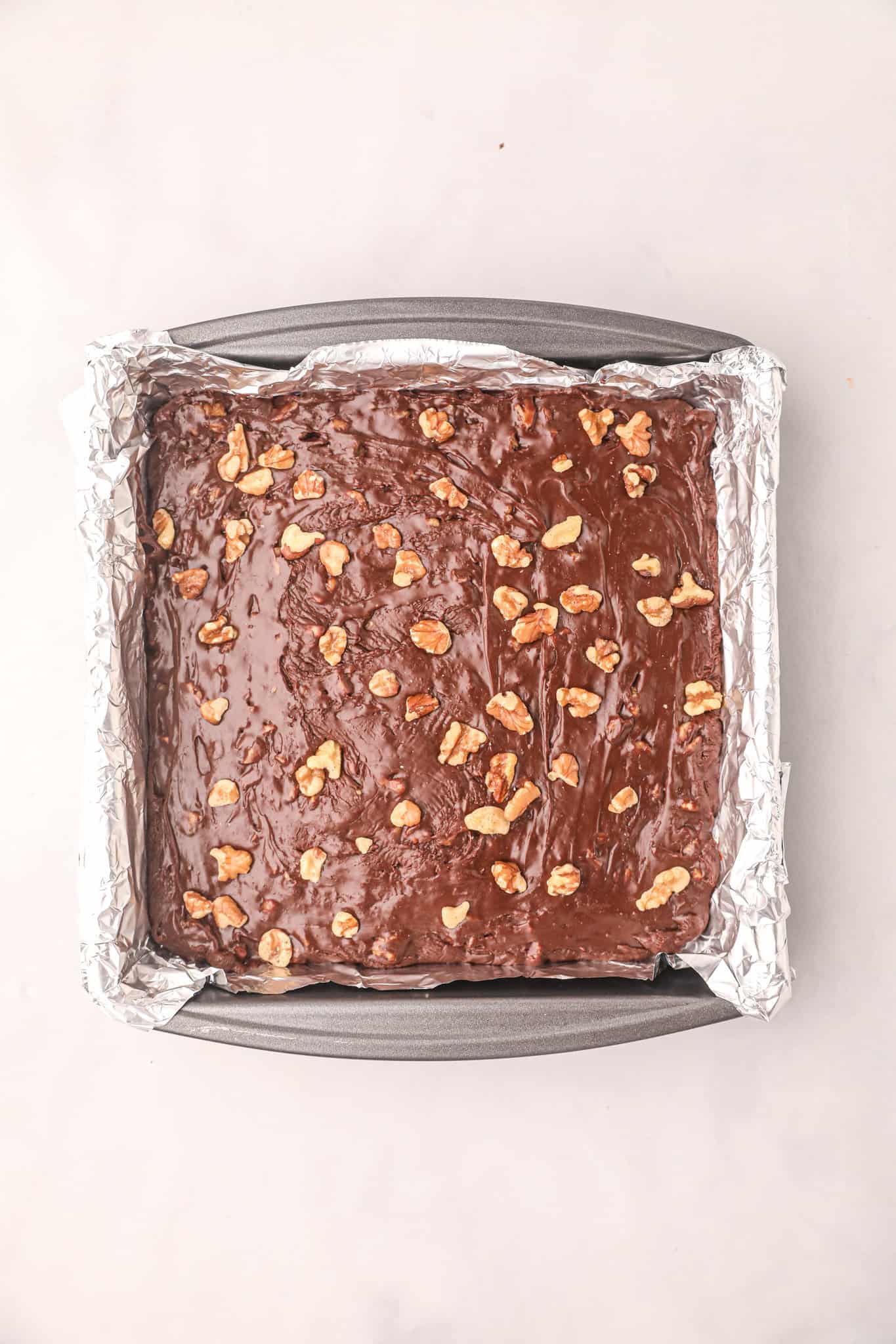 chopped walnuts sprinkled on top of chocolate fudge mixture in a foil lined pan