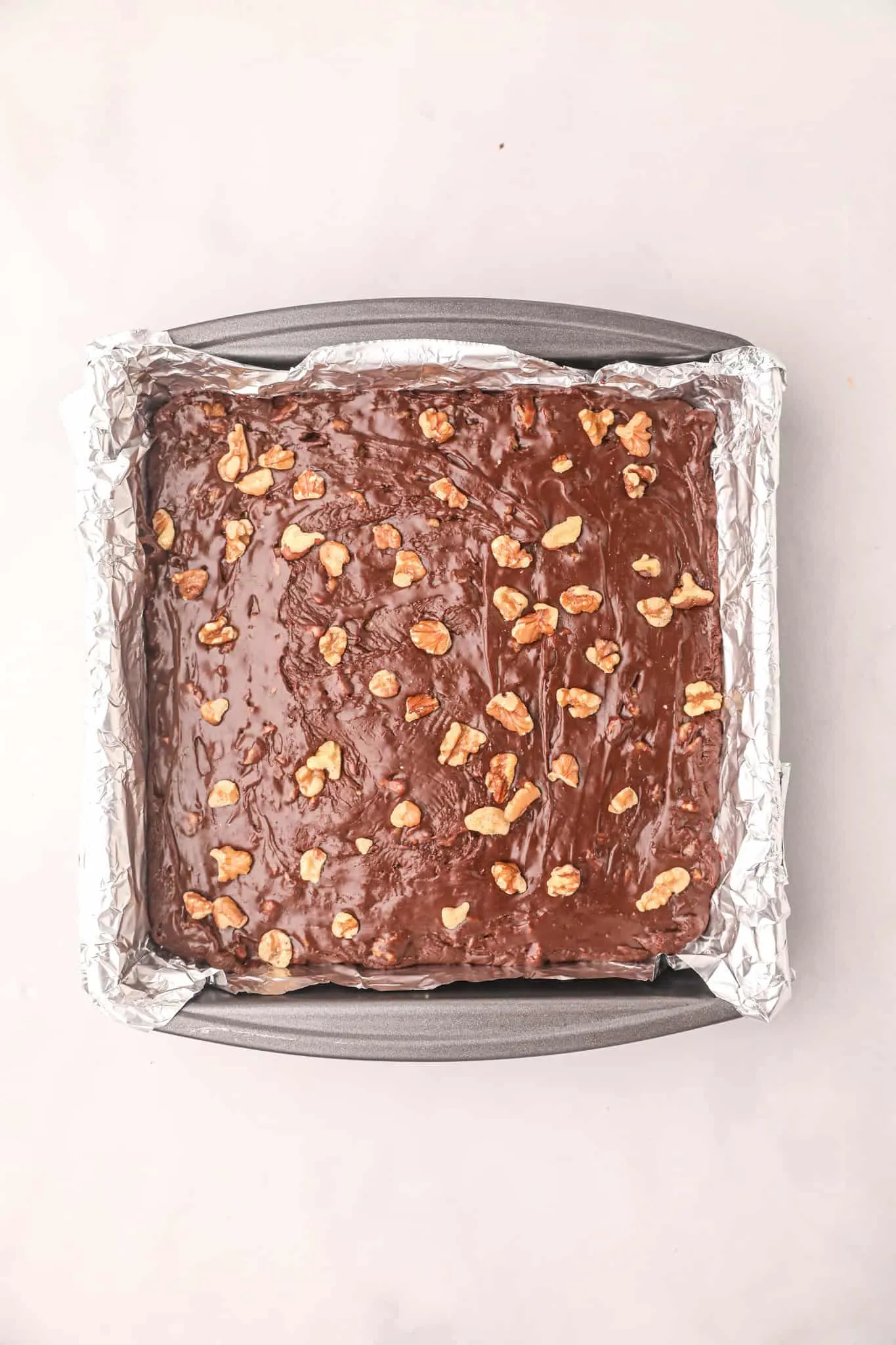 chopped walnuts sprinkled on top of chocolate fudge mixture in a foil lined pan