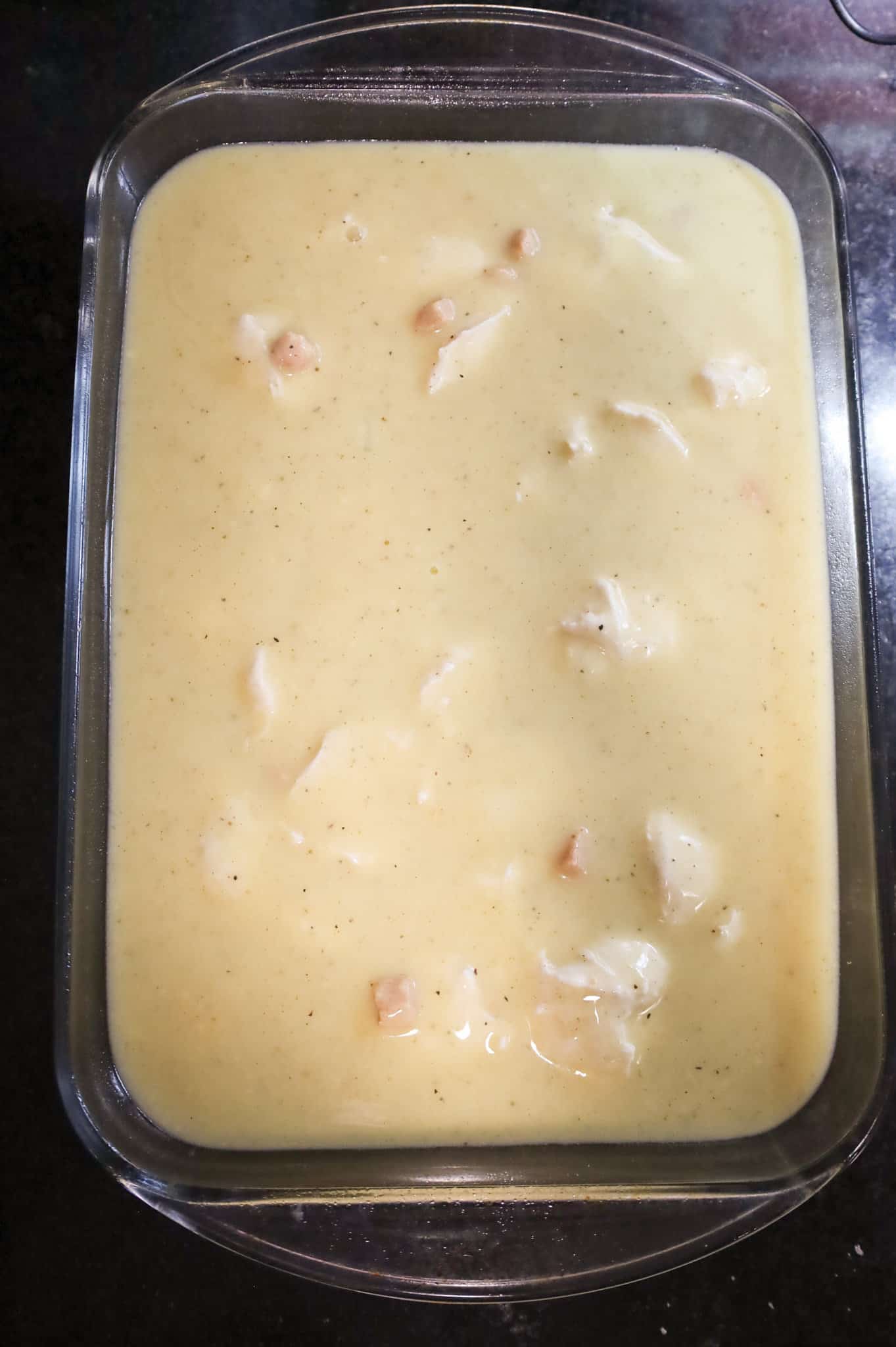 cream of chicken soup mixture poured over chicken and dumpling mixture in a baking dish