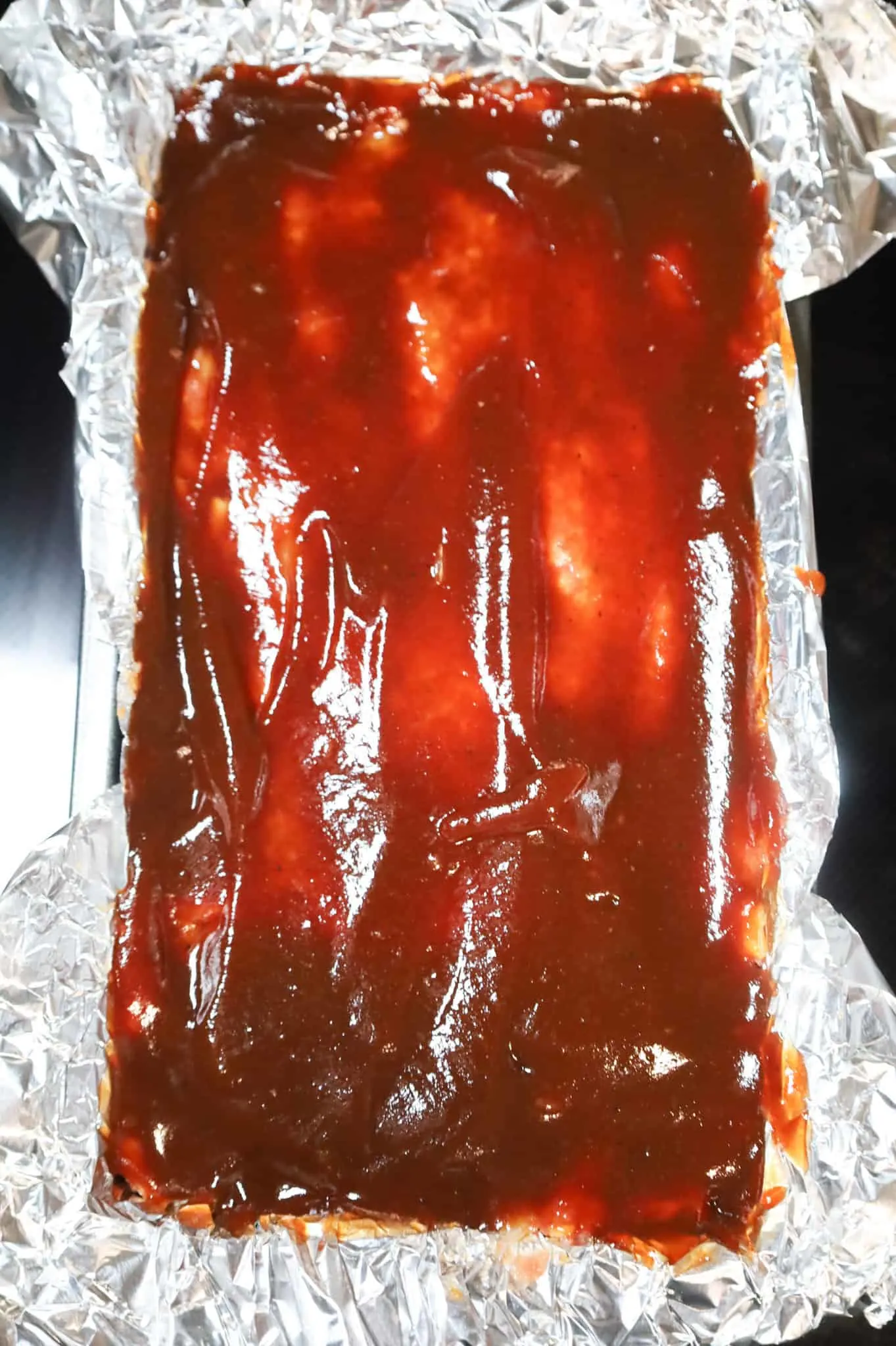 BBQ sauce spread on top of meatloaf mixture in a loaf pan
