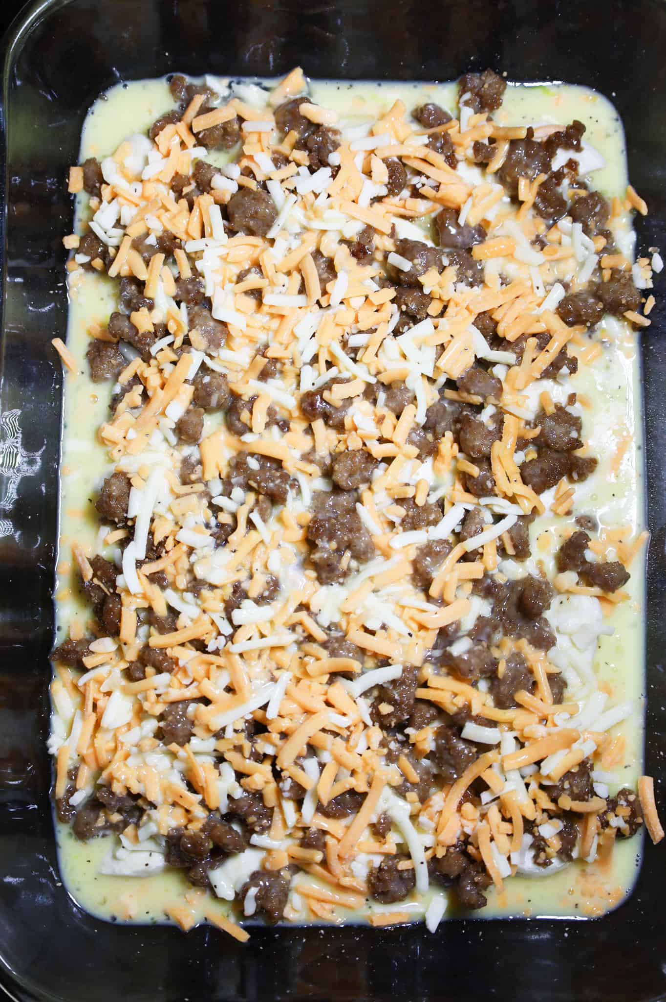 shredded cheese on top of sausage and biscuits in a baking dish with egg mixture