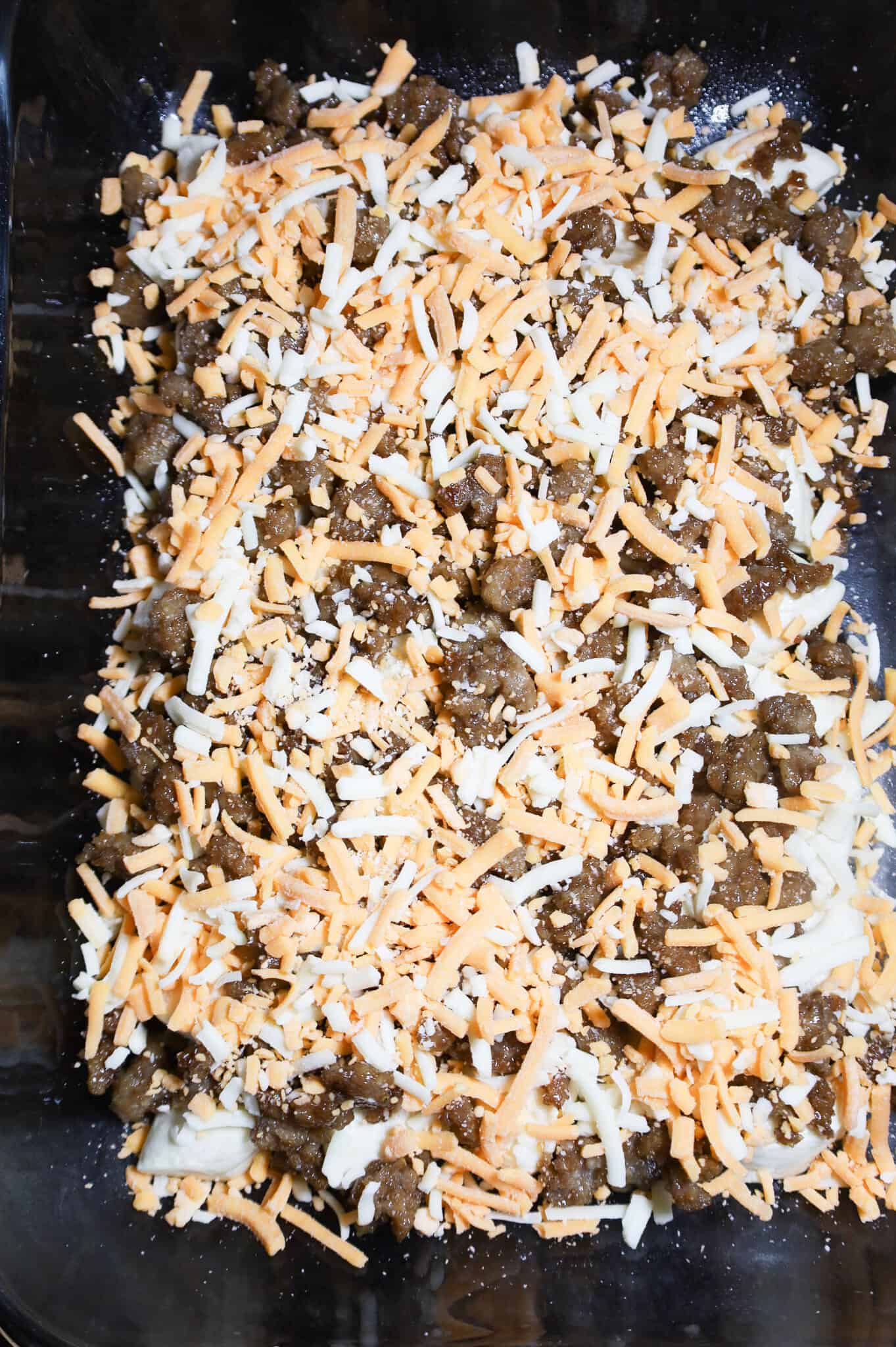 shredded cheese and sausage crumble on top of biscuit pieces in a baking dish