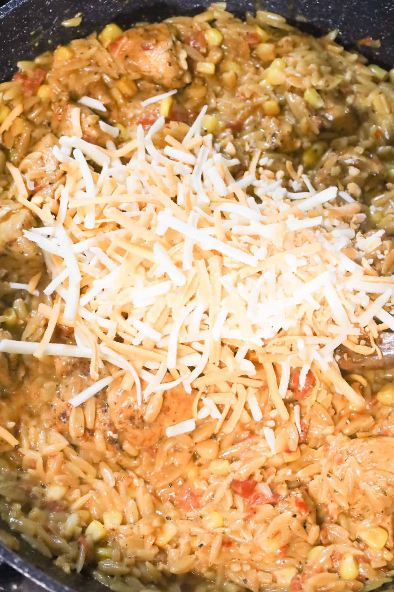 shredded cheese on top of cajun orzo pasta in a skillet