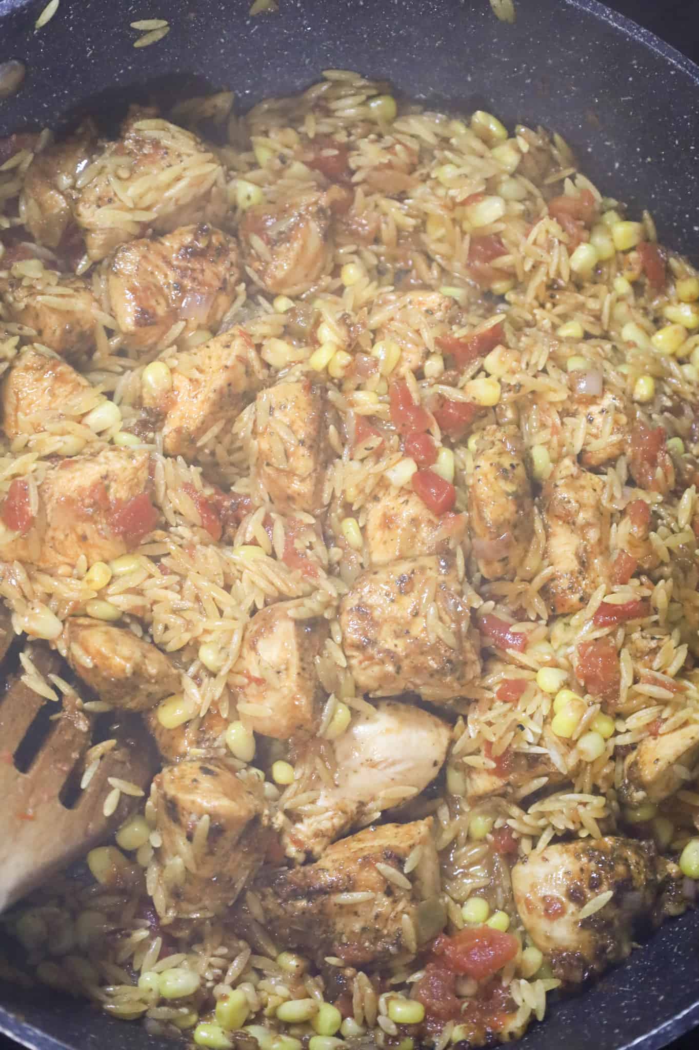 corn and Rotel being stirred with chicken and orzo pasta in a skillet