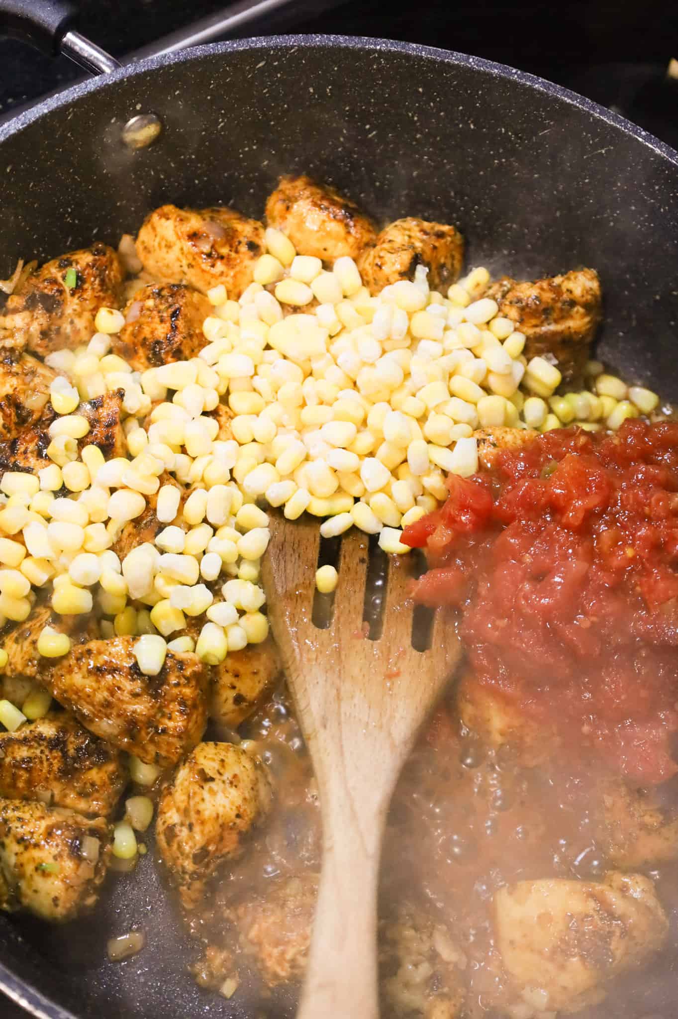 frozen corn kernels and Rotel on top of cooked chicken breast chunks in a skillet