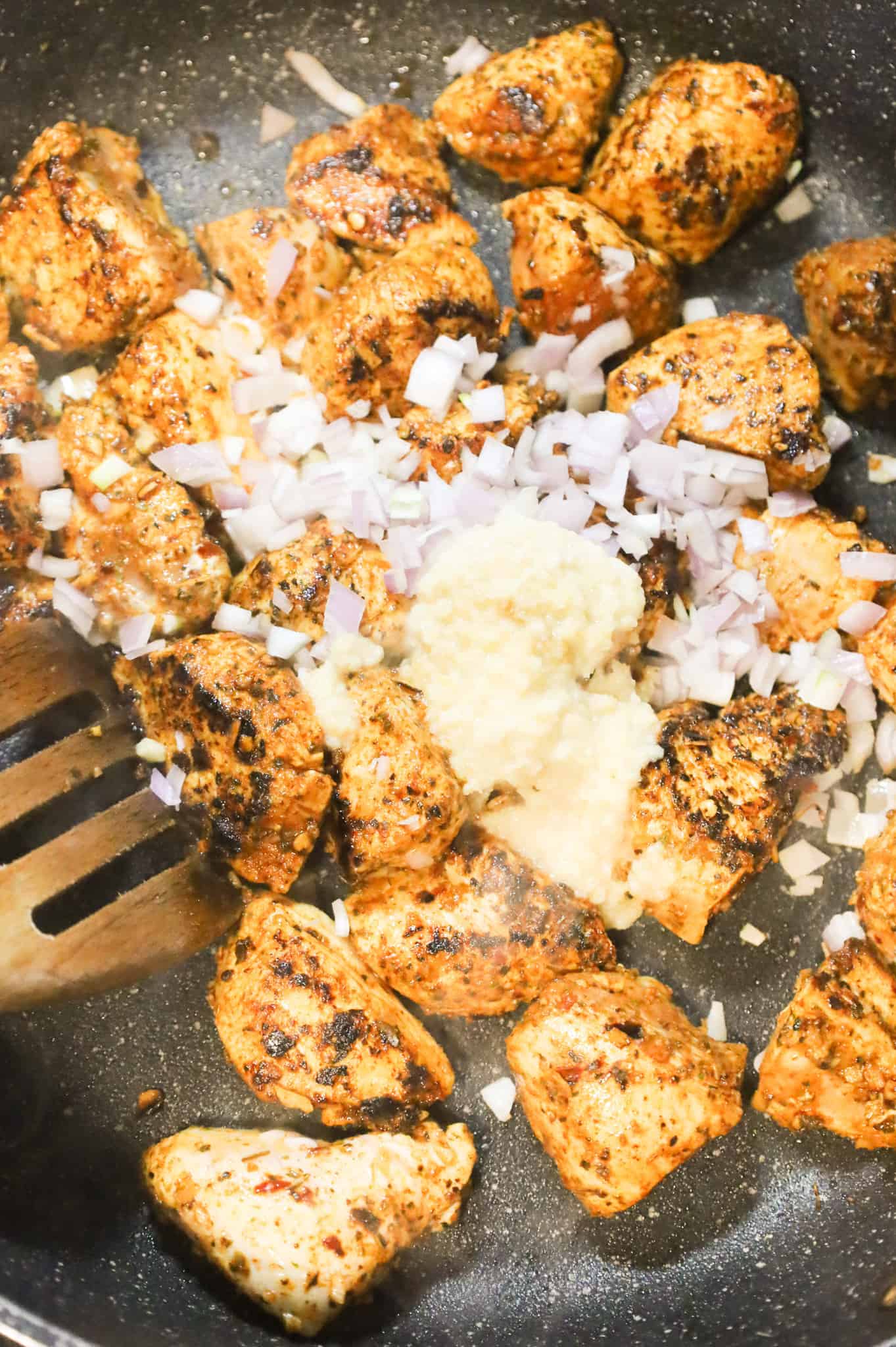 minced shallots and garlic puree added to a skillet with Cajun chicken breast chunks