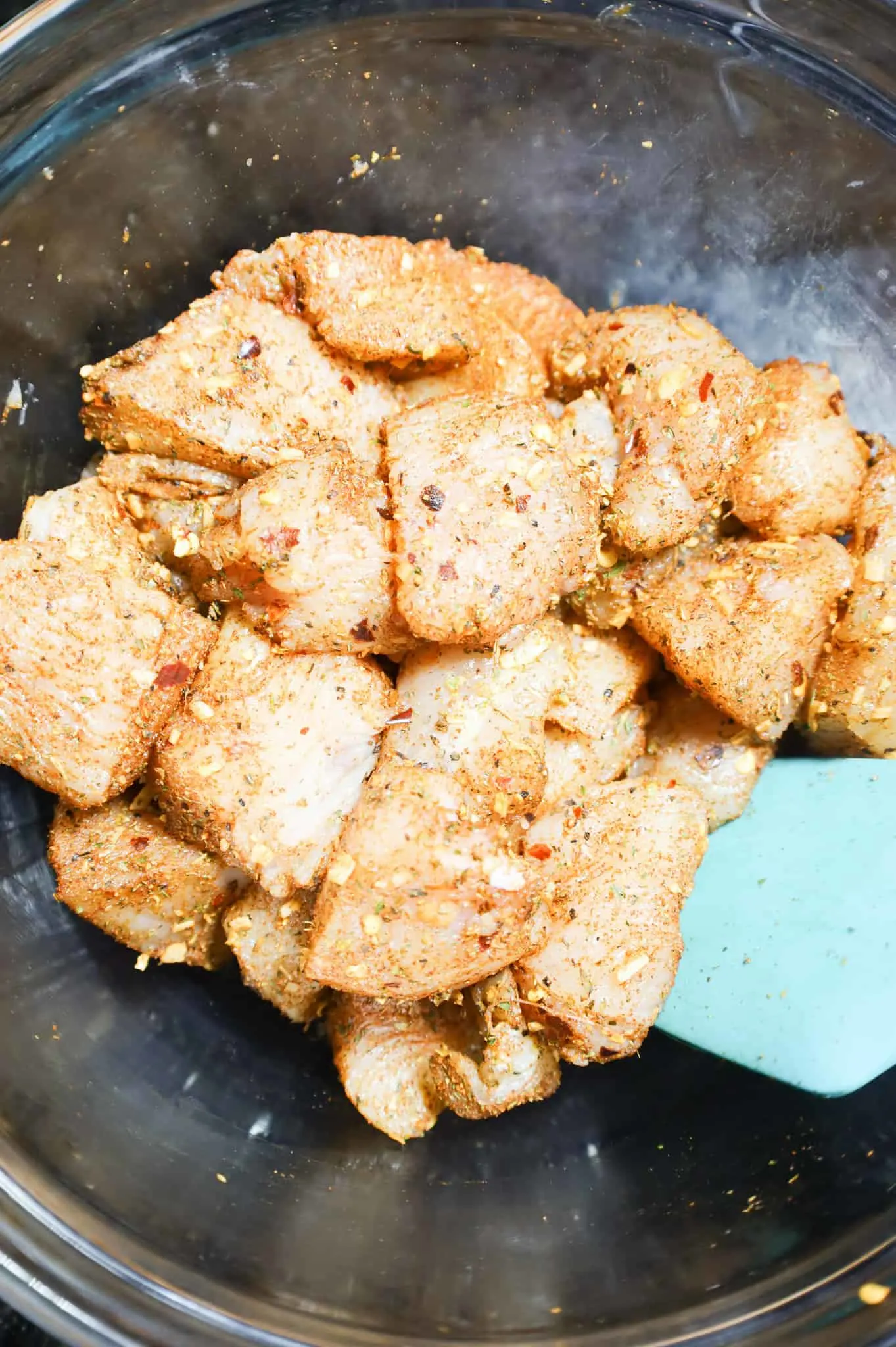 chicken breast chunks being tossed with Cajun seasoning in a bowl