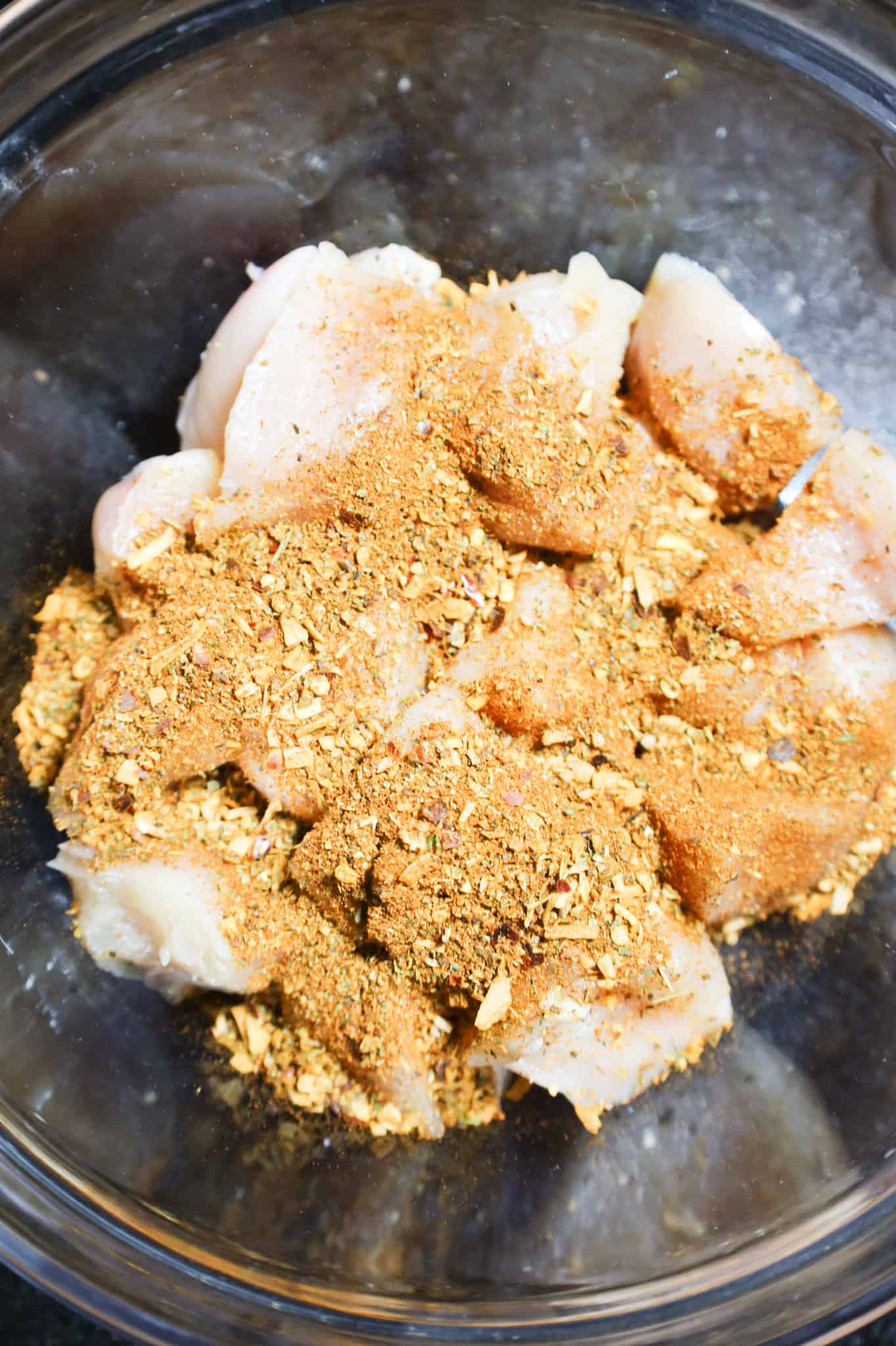 cajun seasoning on top of raw chicken breast chunks in a bowl