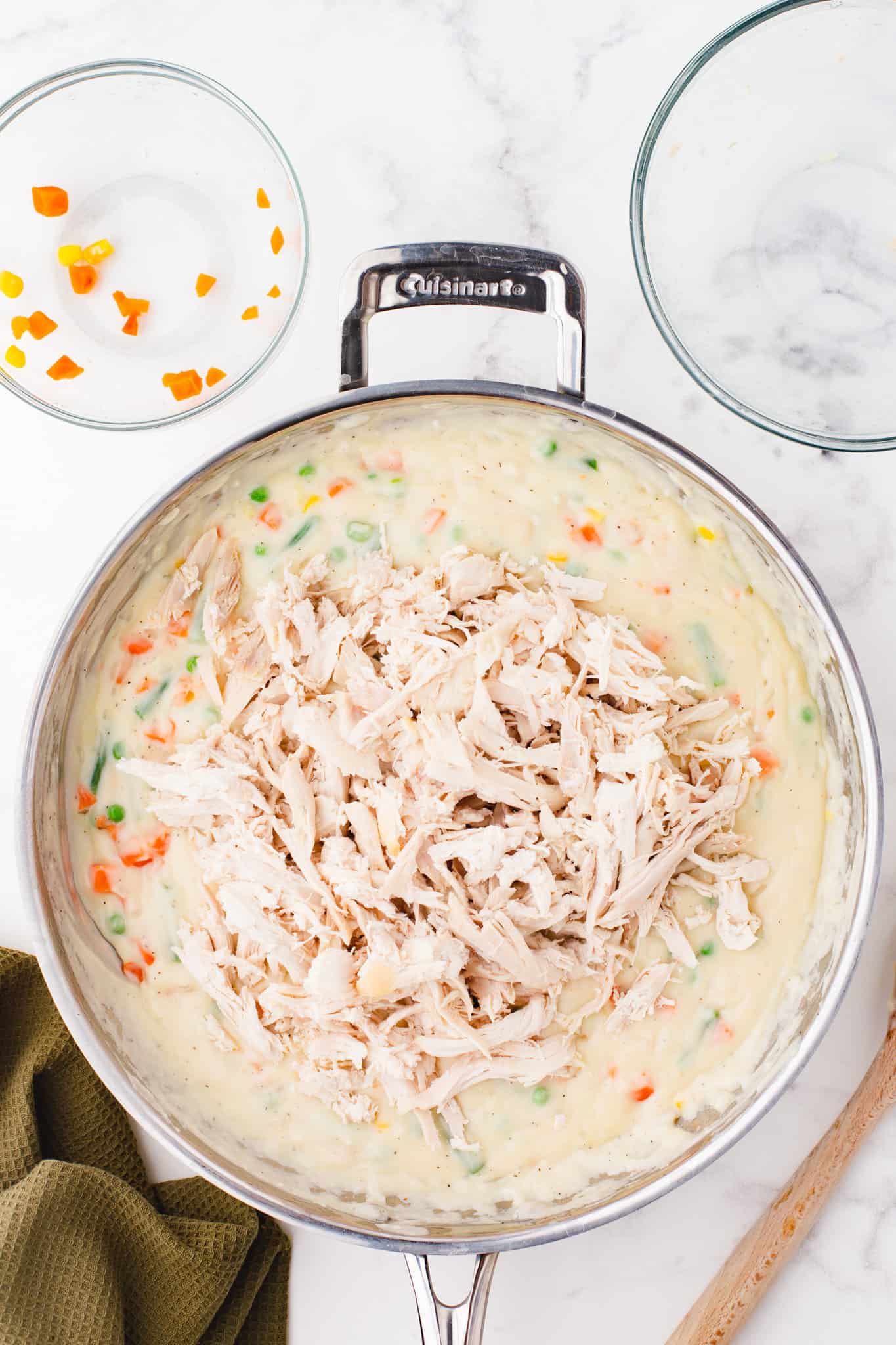shredded chicken added to creamy vegetable mixture in a skillet