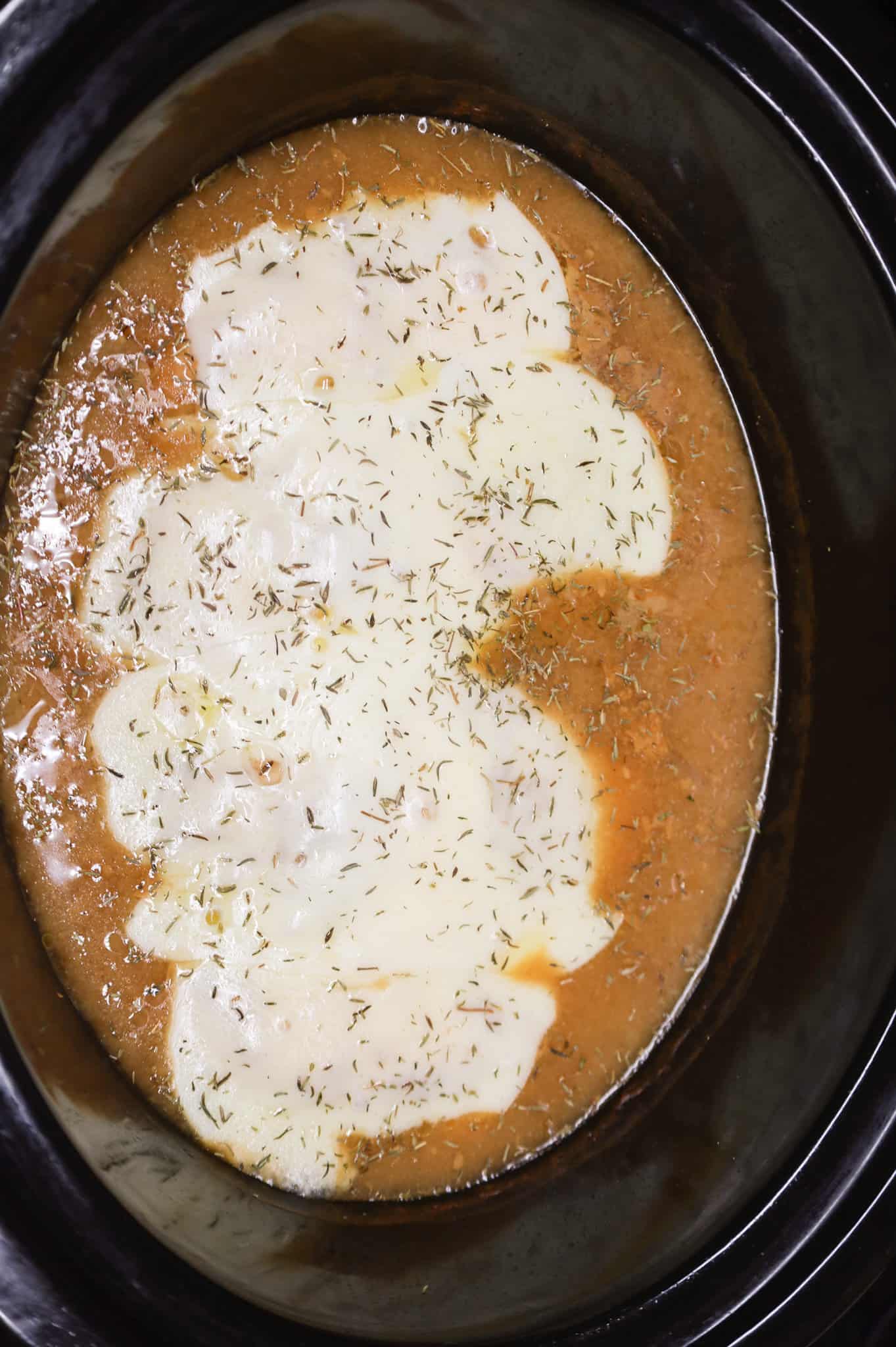 thyme leaves sprinkled on top of French onion chicken in a crock pot
