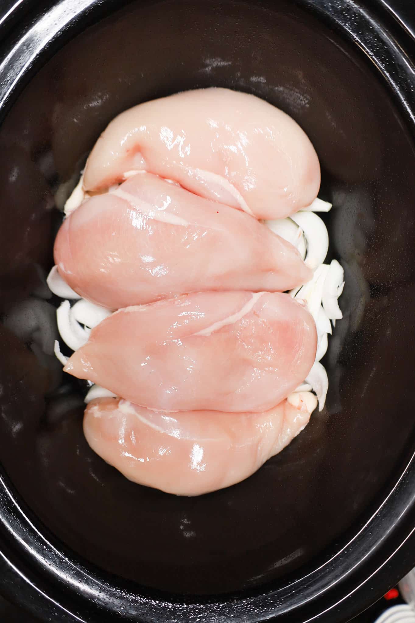boneless, skinless chicken breasts on top of onion slices in a crock pot
