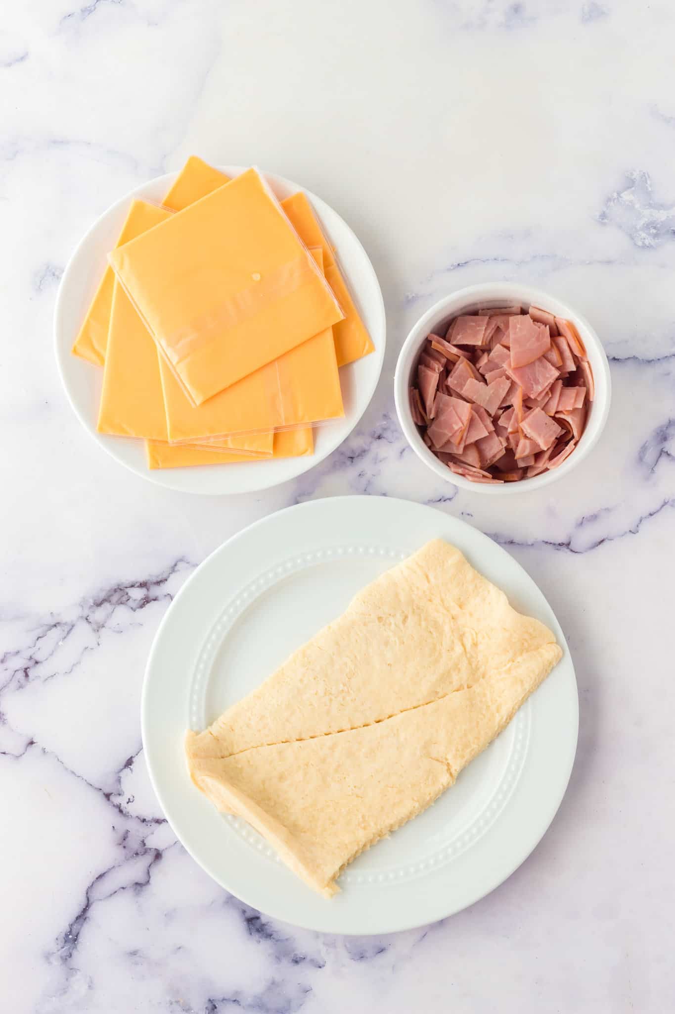 rectangle of crescent dough, cheese slices and chopped ham on the counter