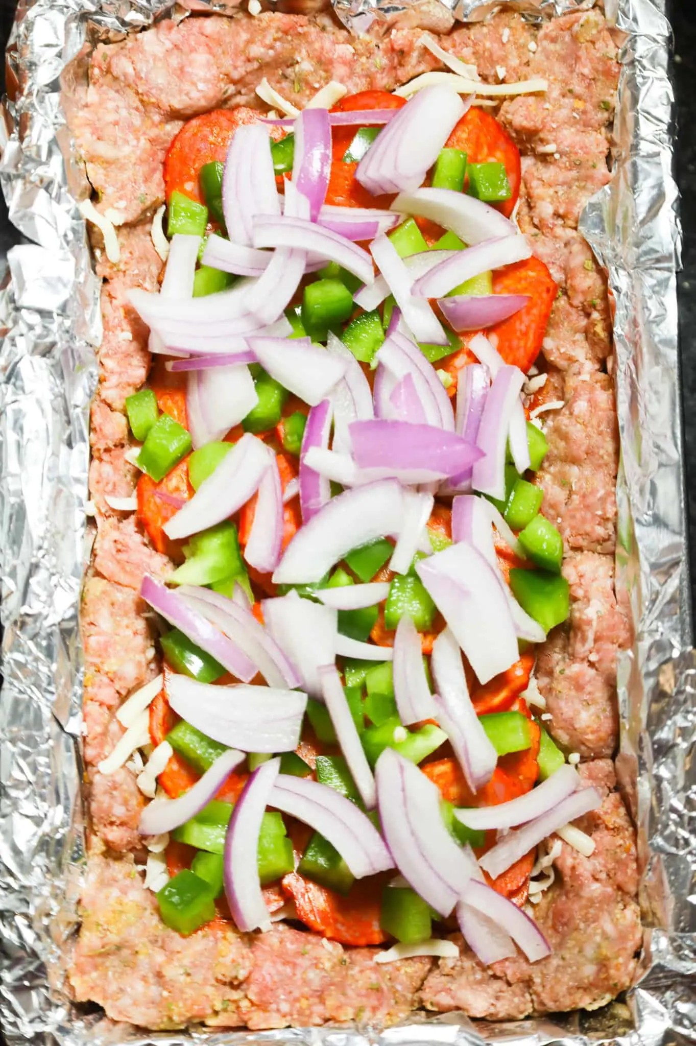 diced red onions, green peppers and pepperoni slices in the center of a meatloaf