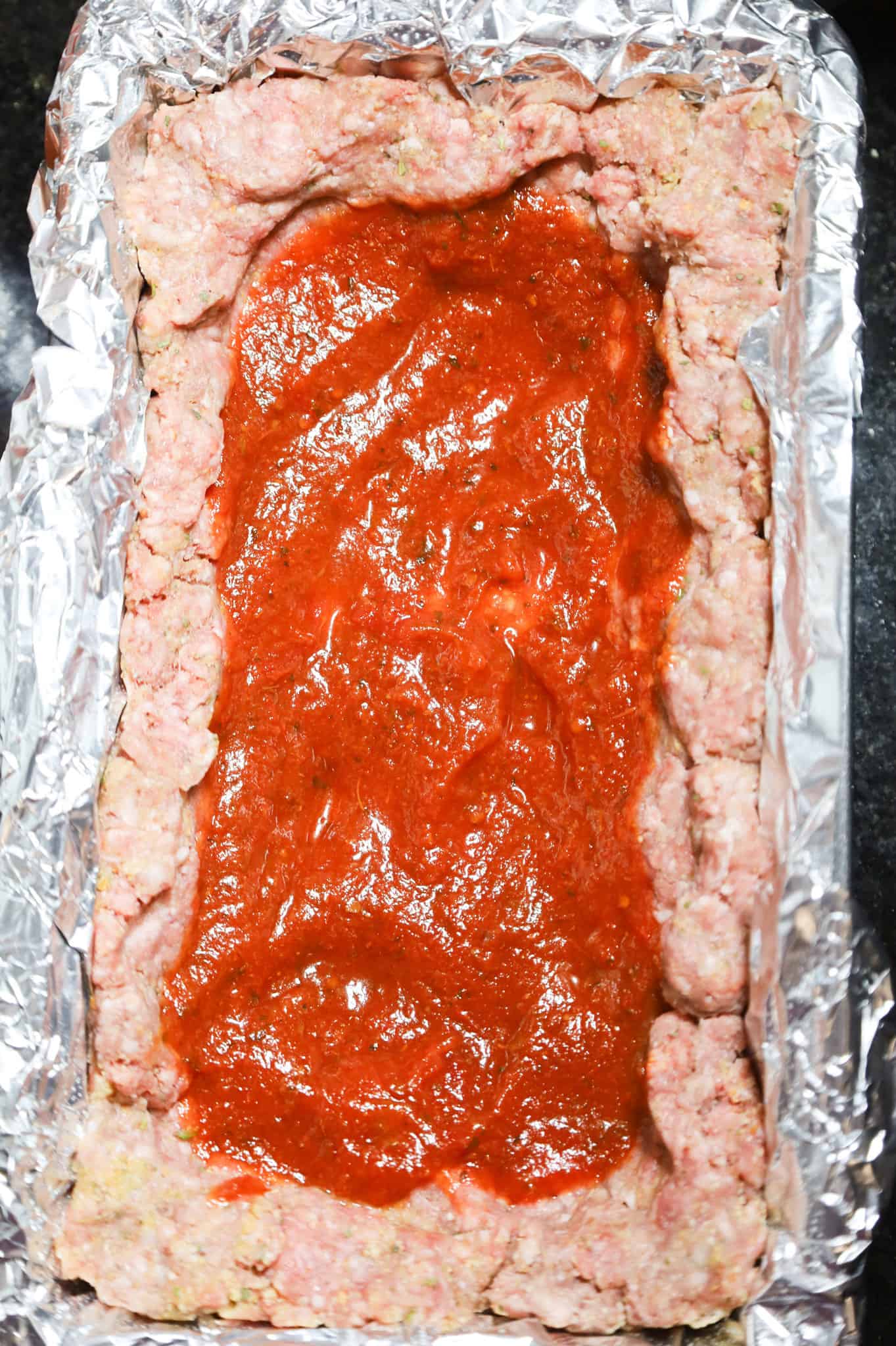 pizza sauce spread in the hollow center of a raw meatloaf