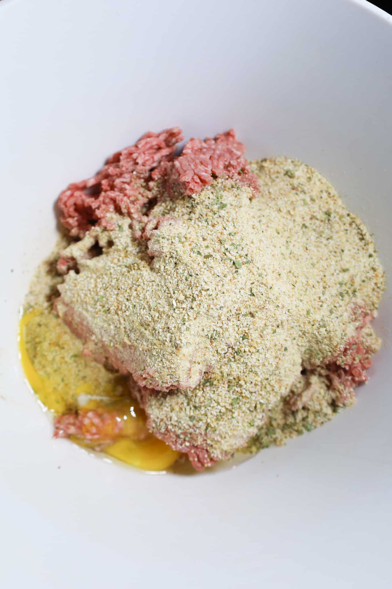 eggs and Italian bread crumbs on top of raw ground beef in a mixing bowl