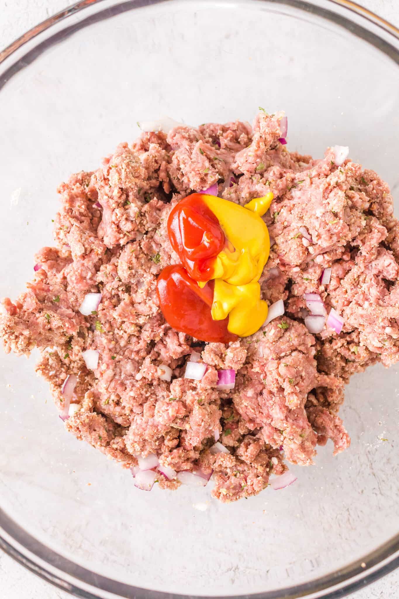 mustard and ketchup on top of ground beef mixture in a mixing bowl