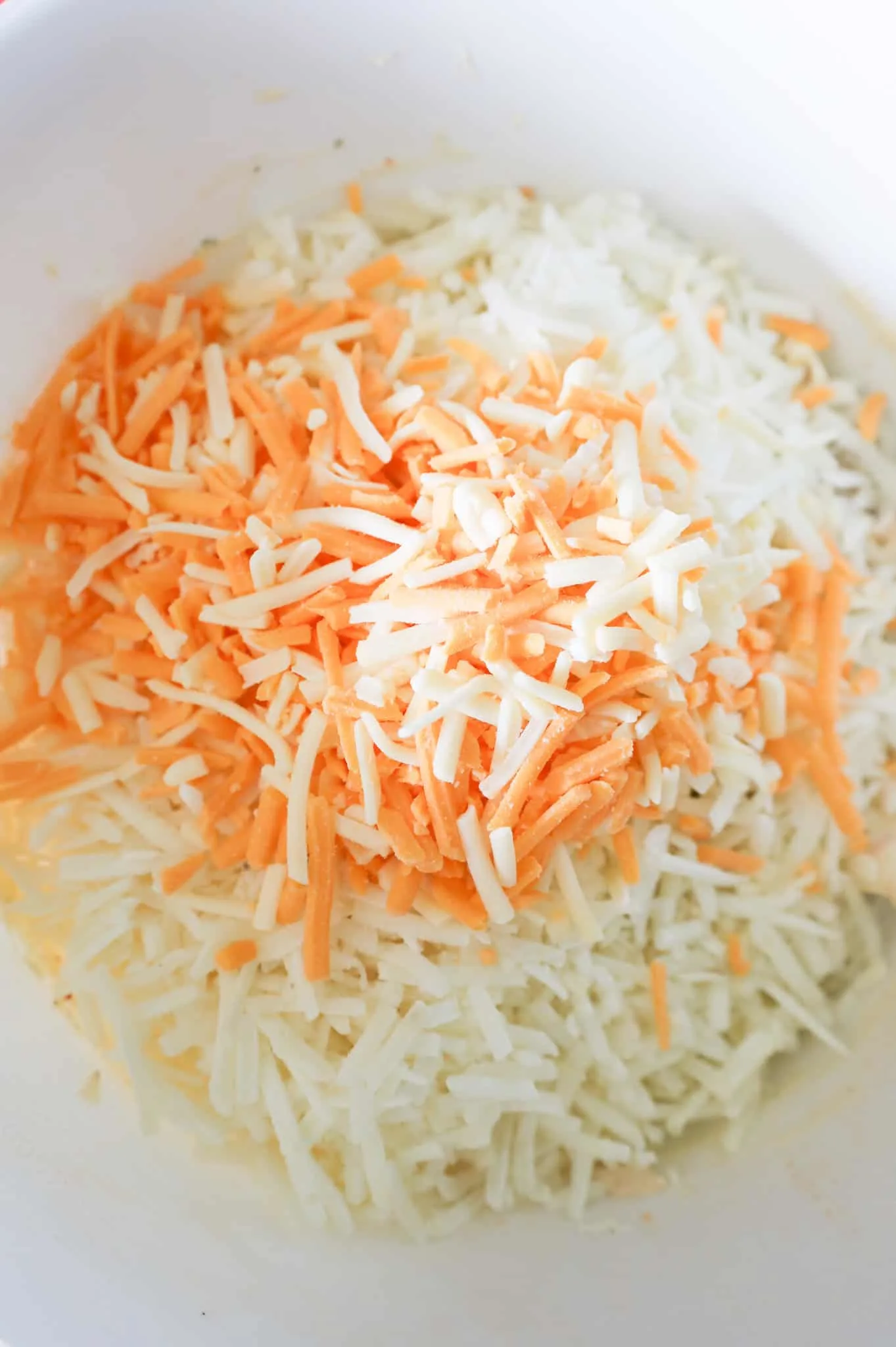 shredded cheddar cheese on top of shredded hashbrown potatoes in a mixing bowl