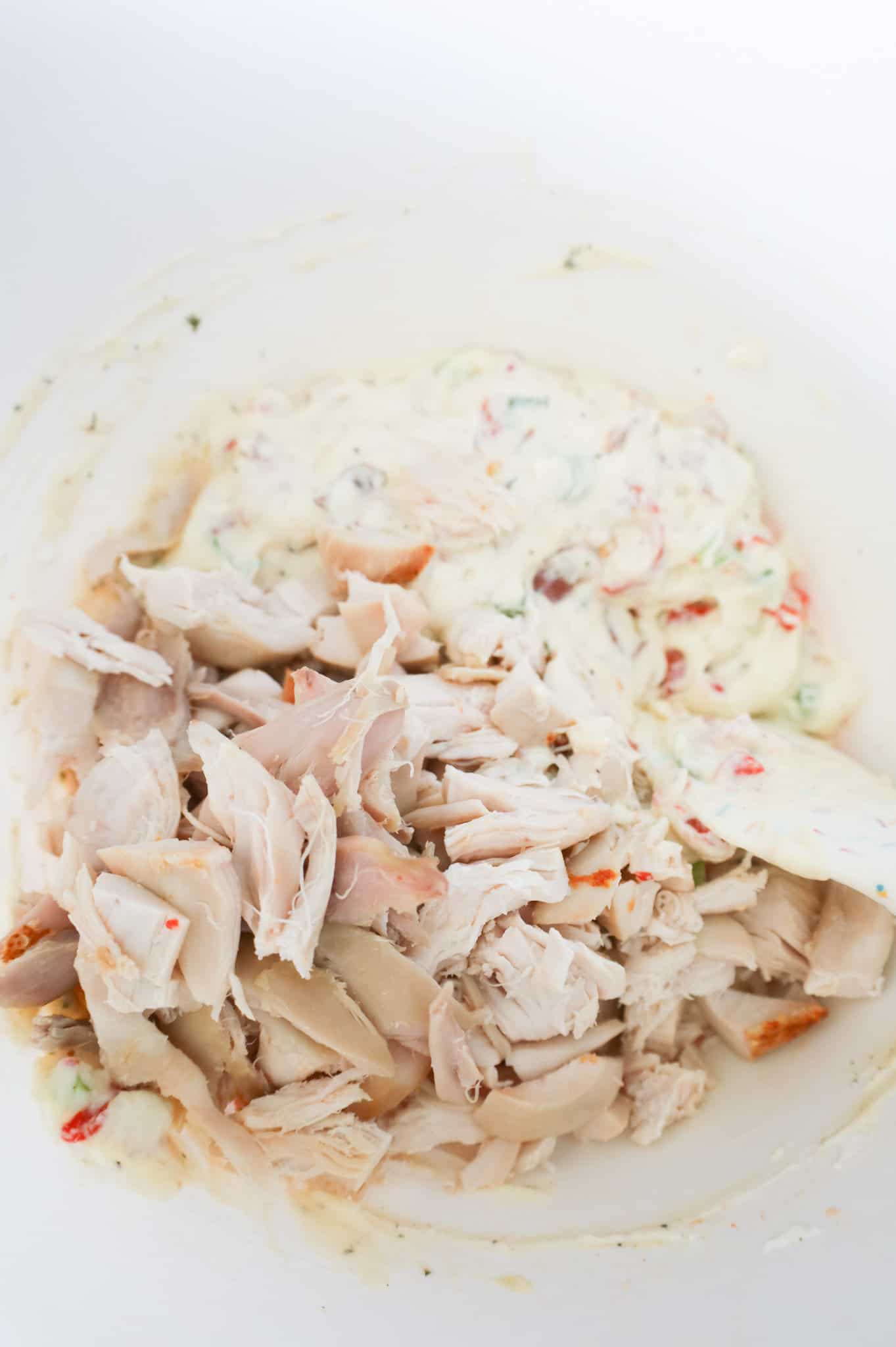 shredded rotisserie chicken on top of creamy mixture in a mixing bowl