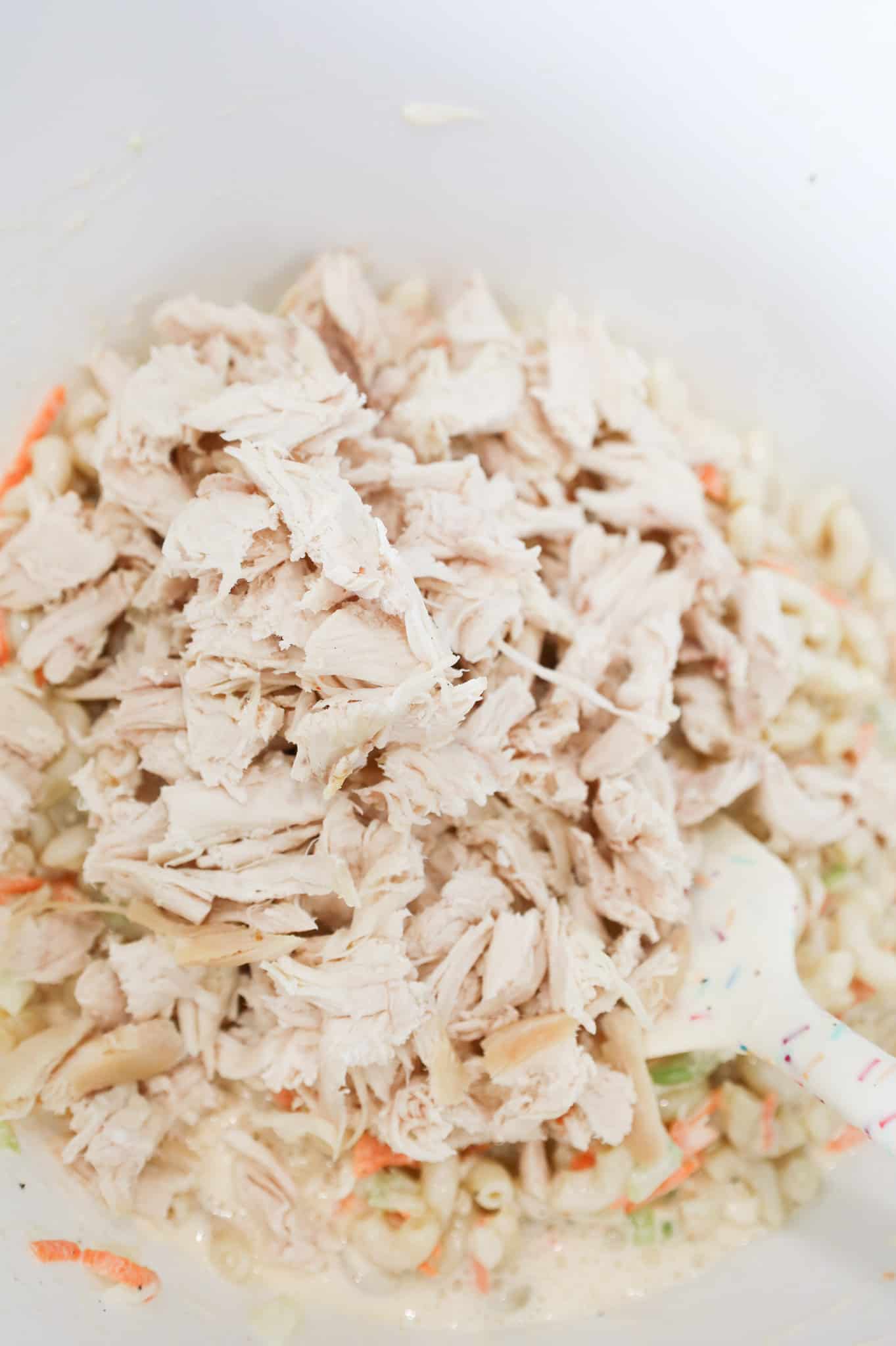 chopped chicken on top of macaroni salad in a mixing bowl