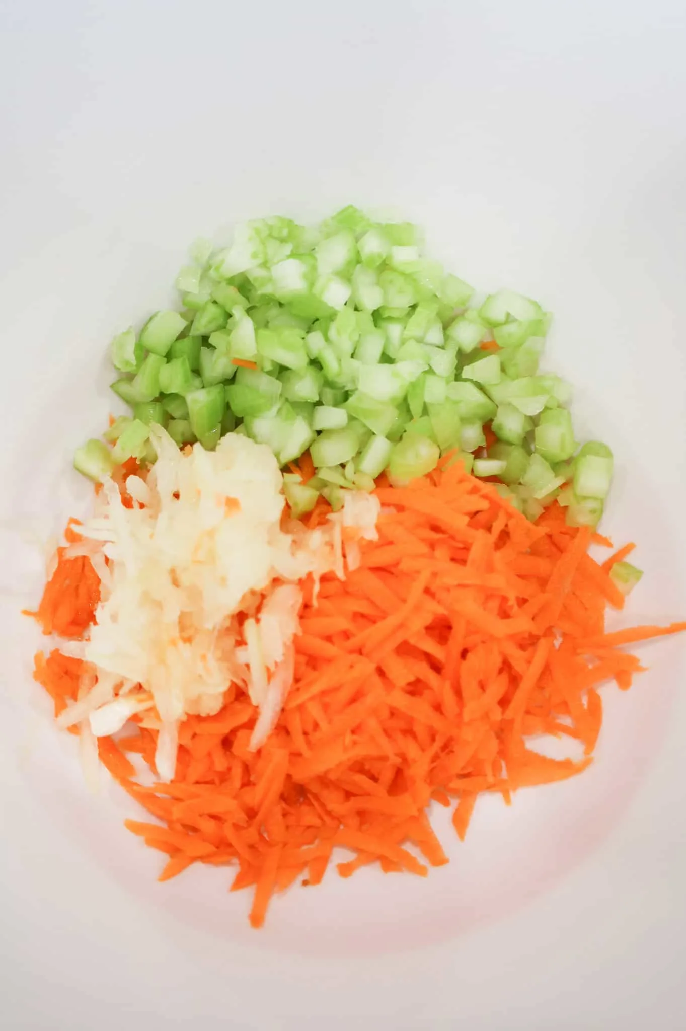 grated onion, carrot and diced celery in a mixing bowl