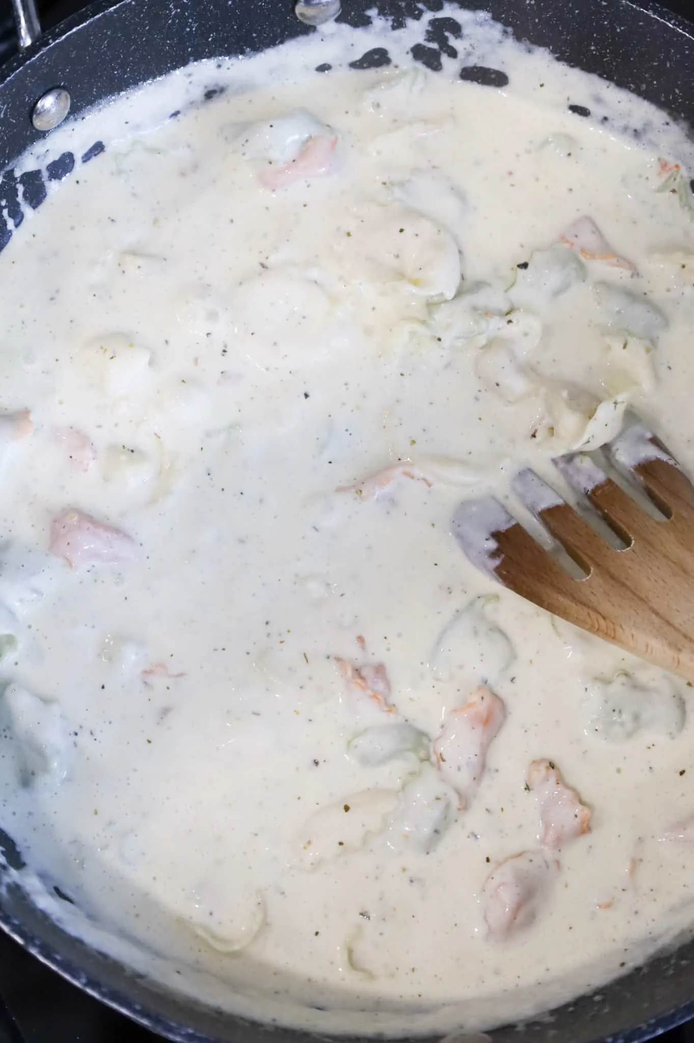 tortellini being stirred in alfredo sauce in a skillet