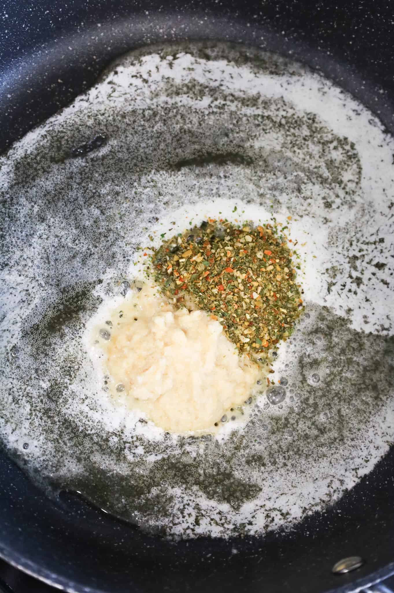 Italian seasoning and garlic puree added to a skillet with melted butter