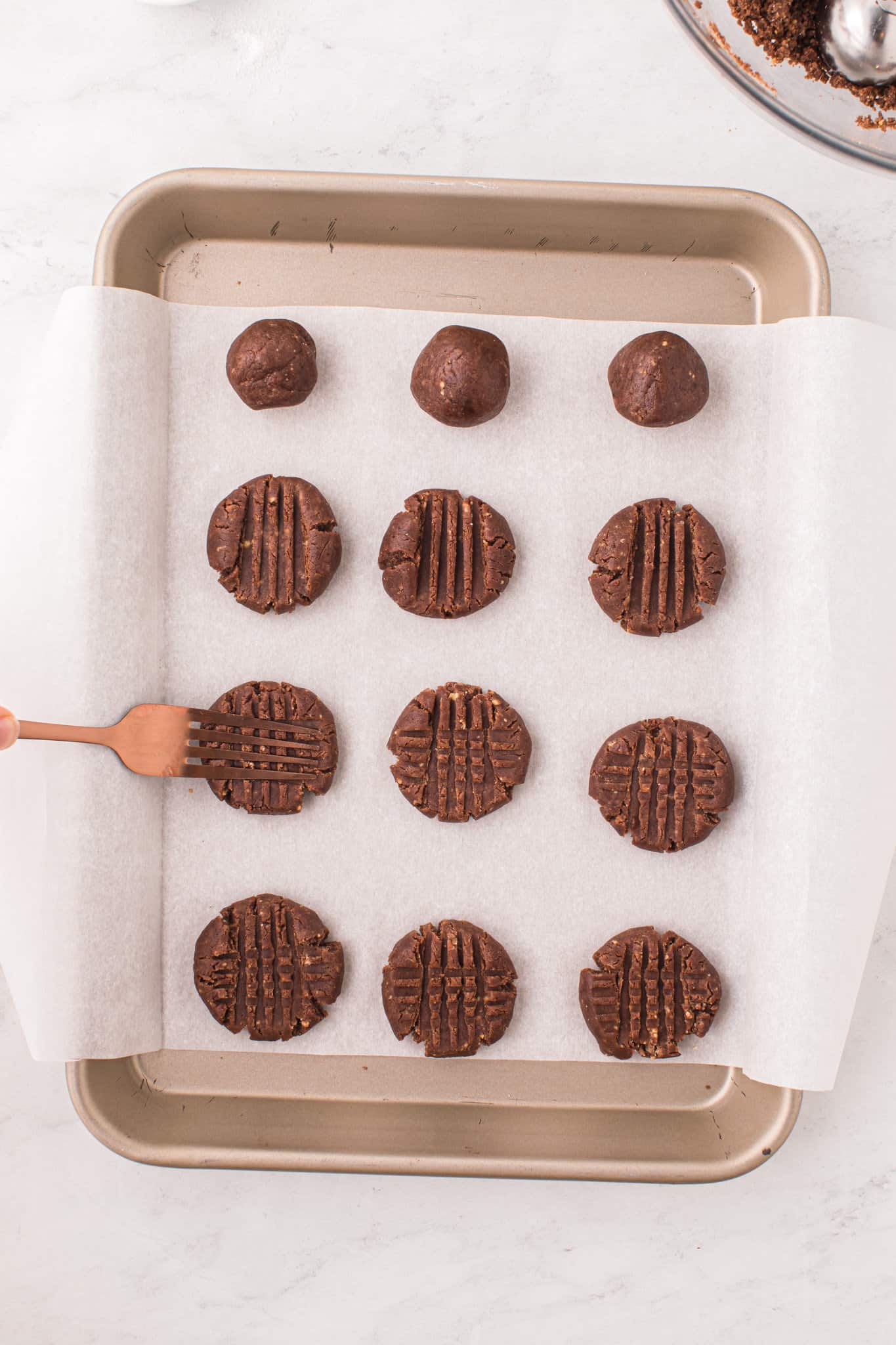 chocolate peanut butter cookie dough balls being pressed down with a fork on a baking sheet