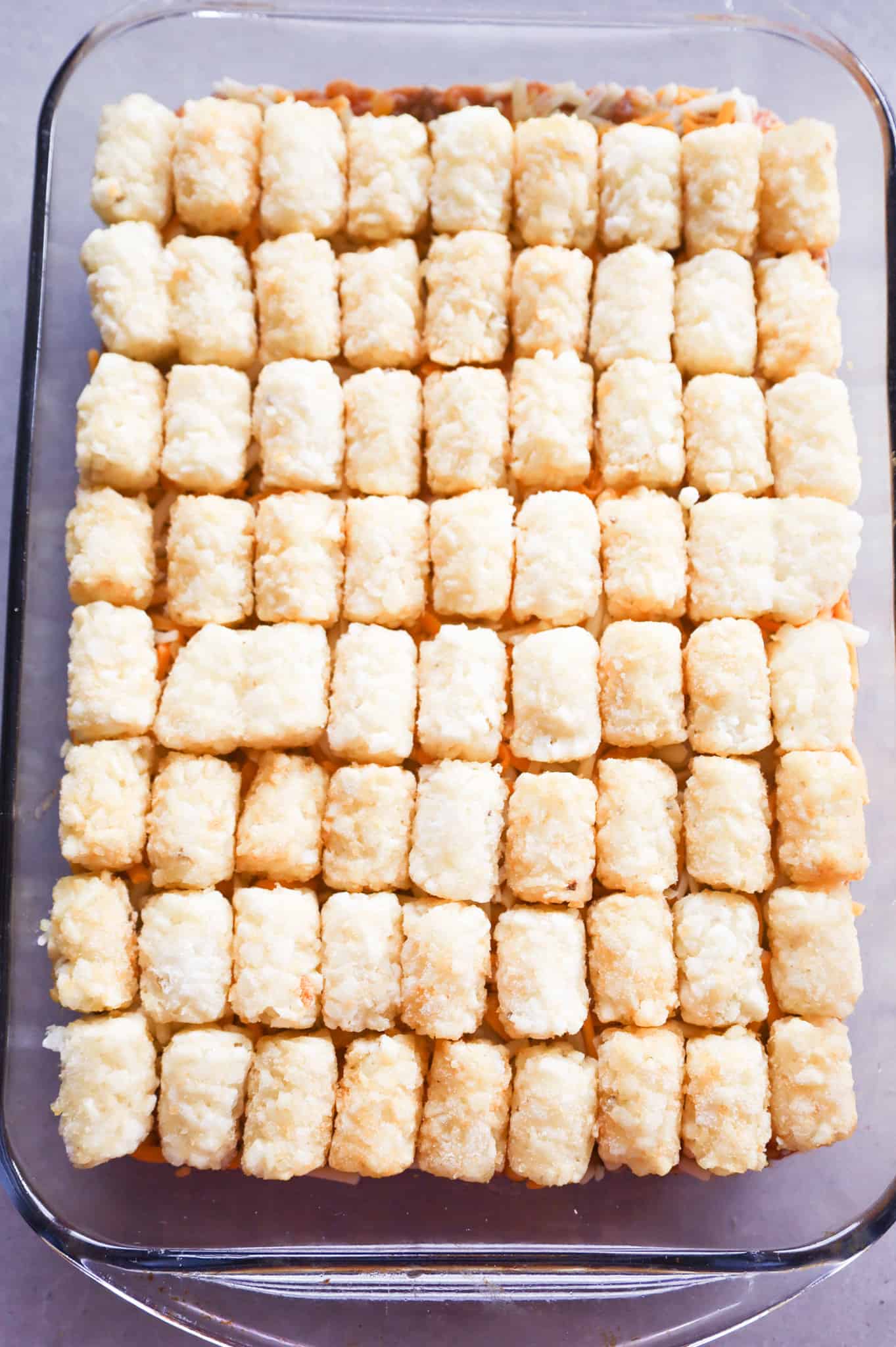 frozen tater tots on top of ground beef mixture in a baking dish