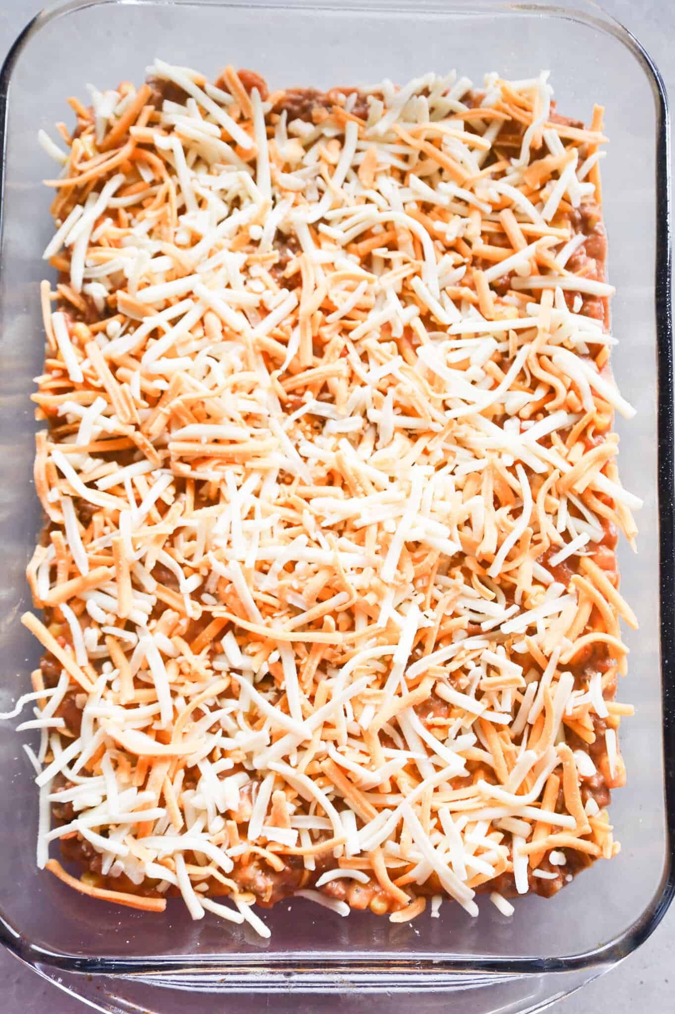 shredded cheese on top of ground beef mixture in a baking dish