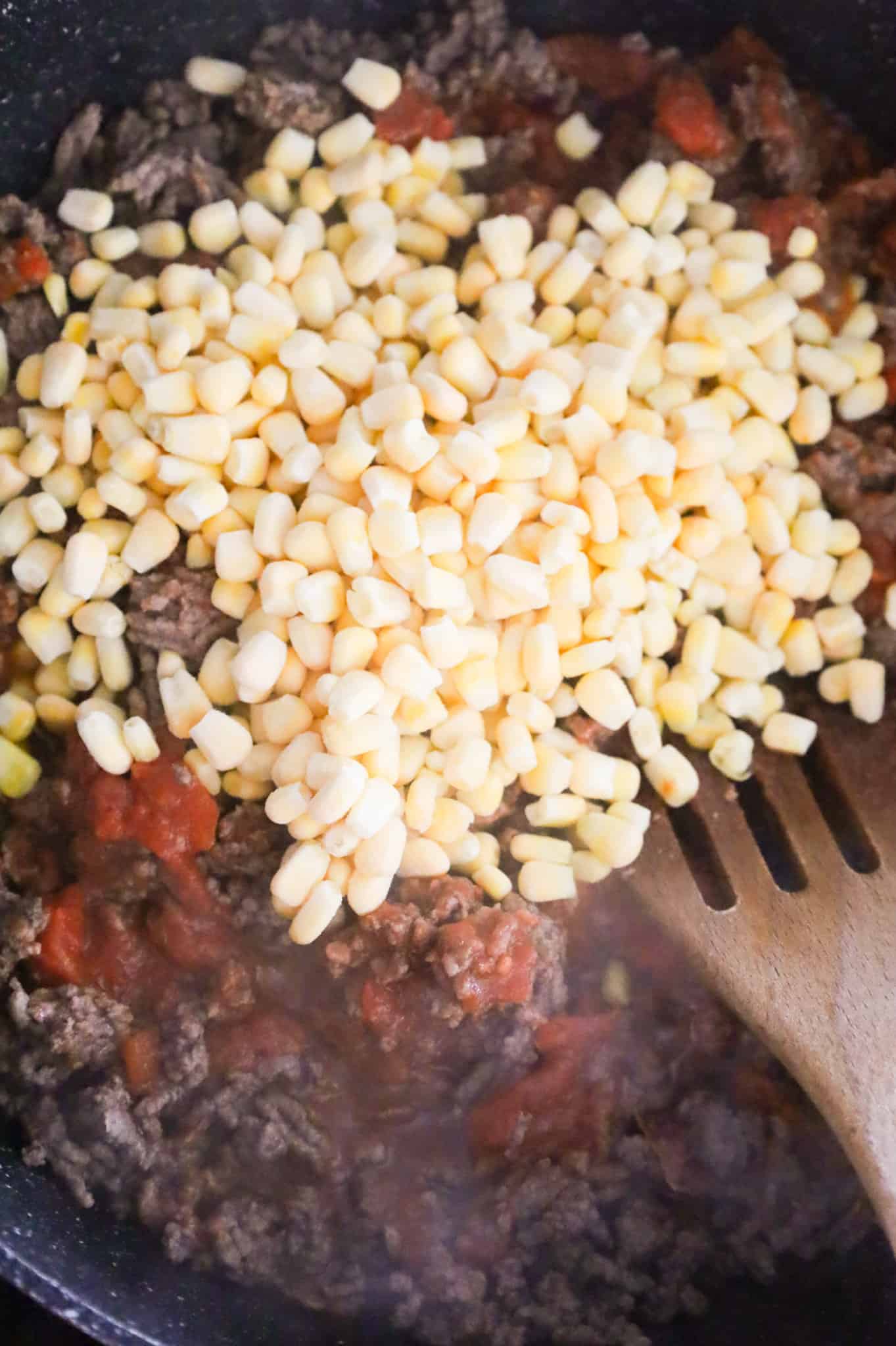 frozen corn kernels on top of ground beef in a skillet