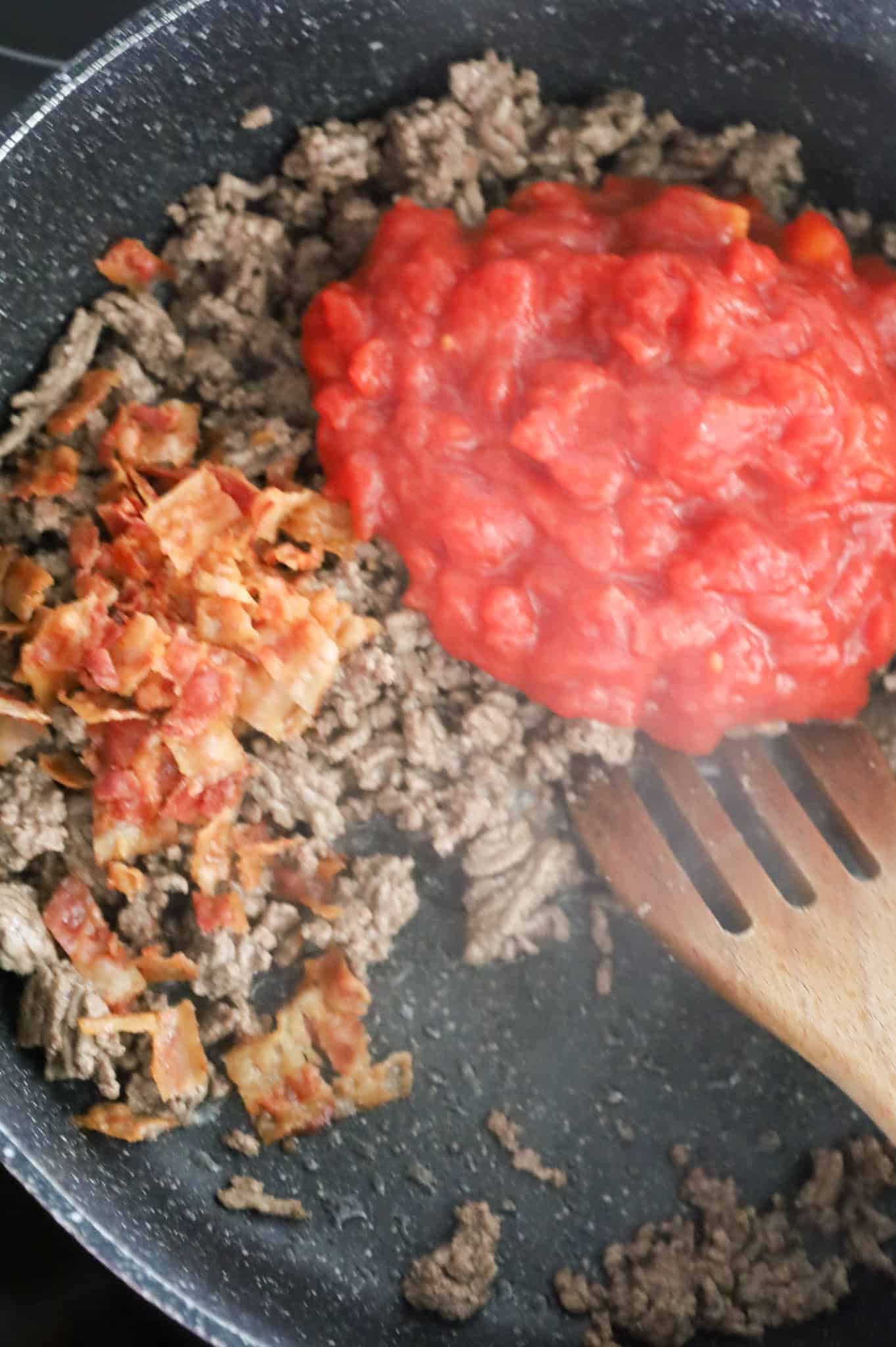 crumbled bacon and diced tomatoes on top of cooked ground beef in a skillet