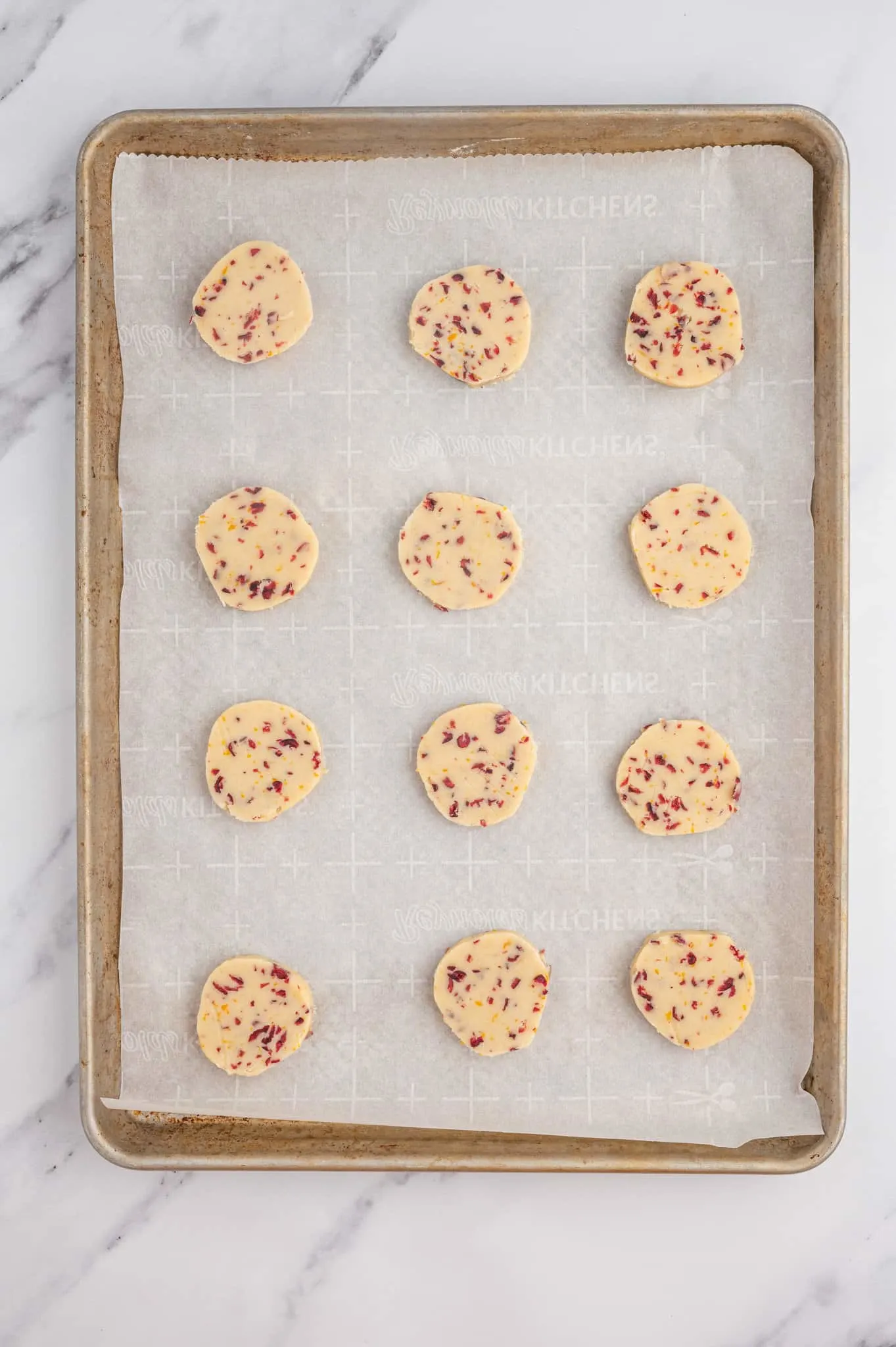 cranberry orange shortbread cookie dough slices on a parchment lined baking sheet