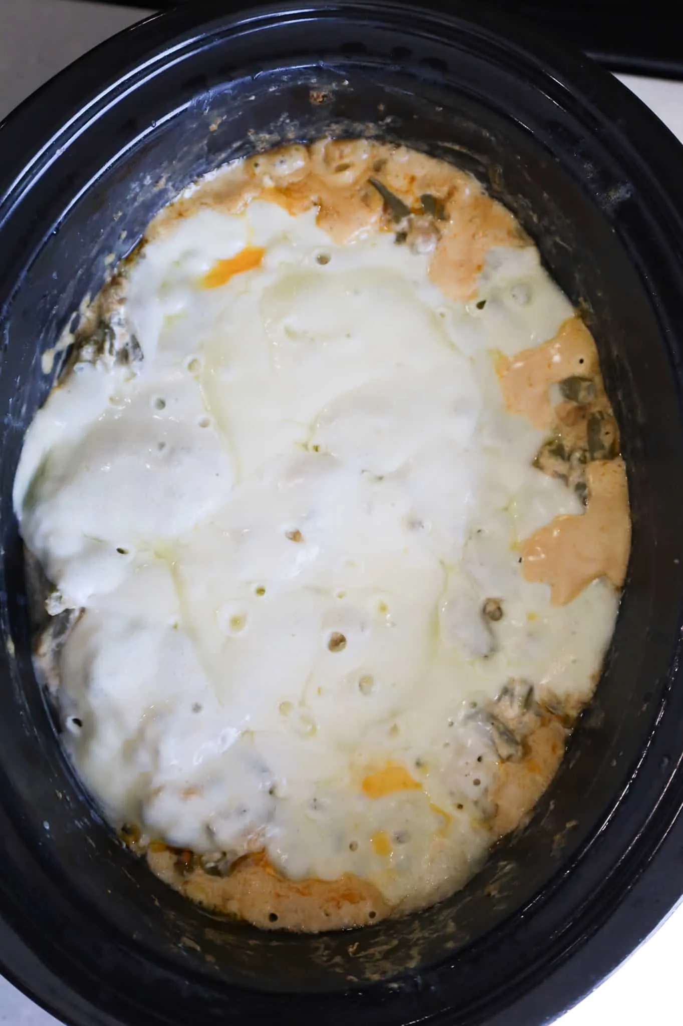 melted provolone cheese on top of green bean casserole in a Crock Pot