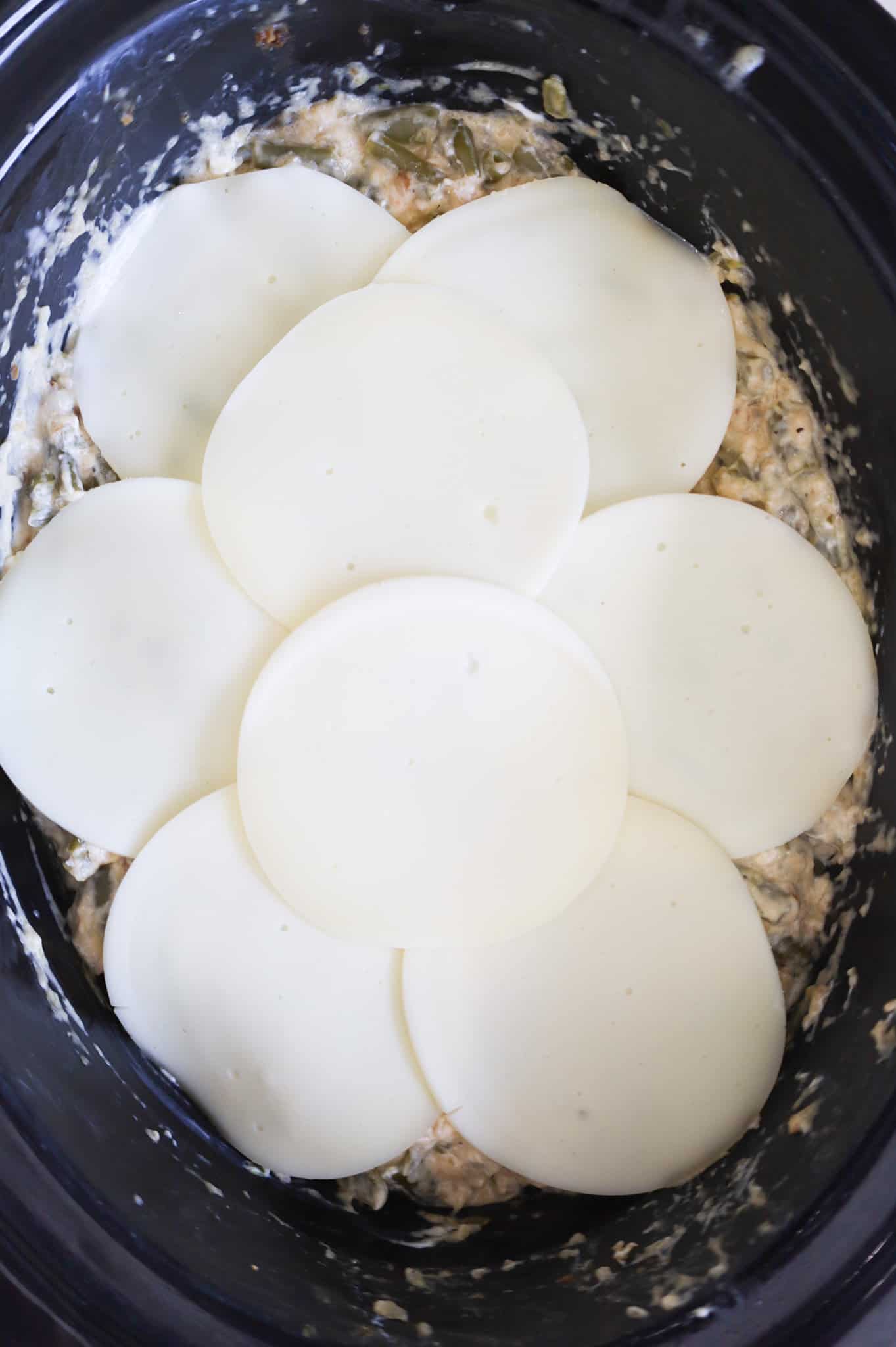 Provolone cheese slices on top of green bean casserole in a slow cooker